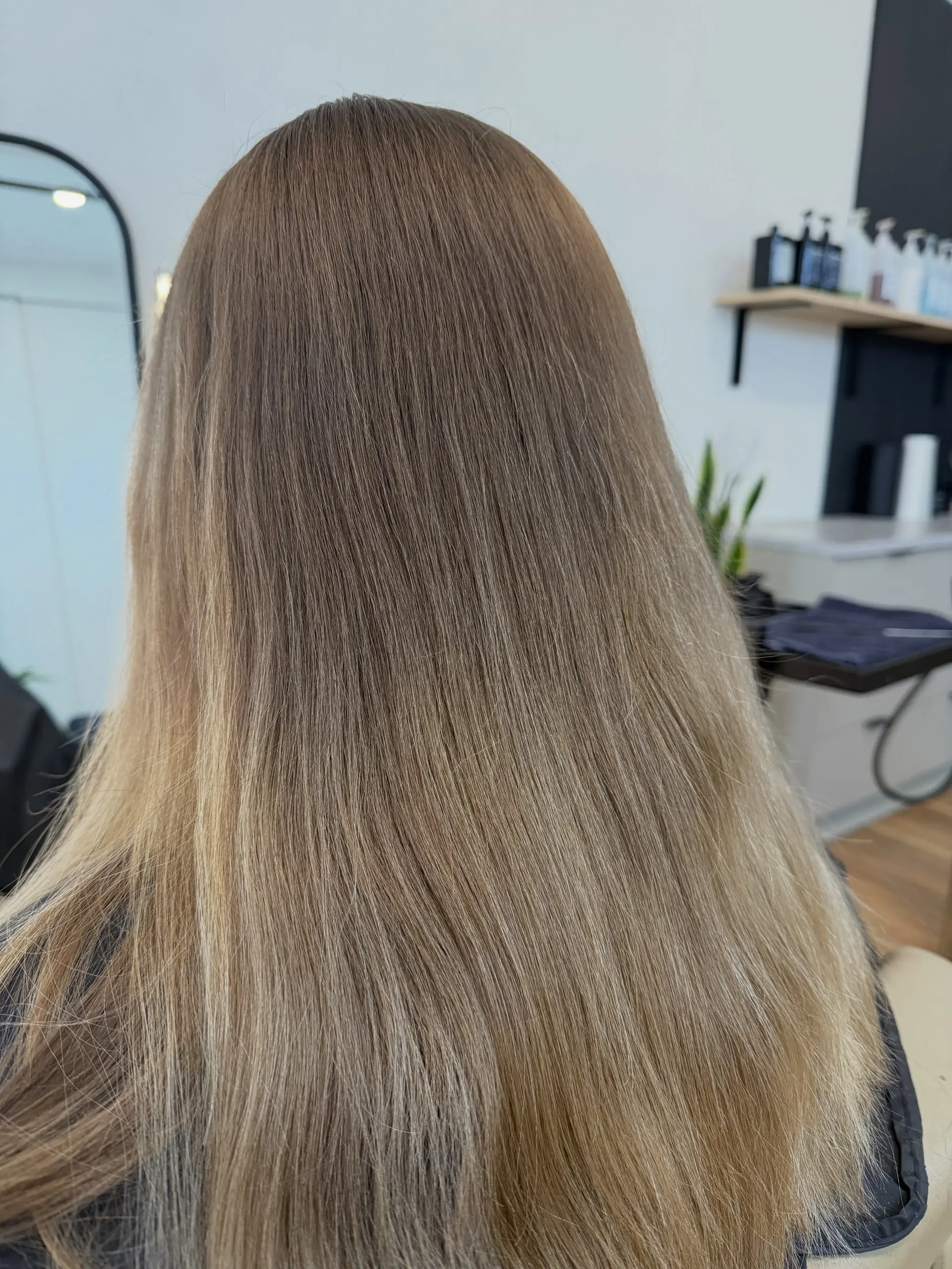 Long straight hair with a seamless blend from a light ash brown root to bright beige blonde ends. 1