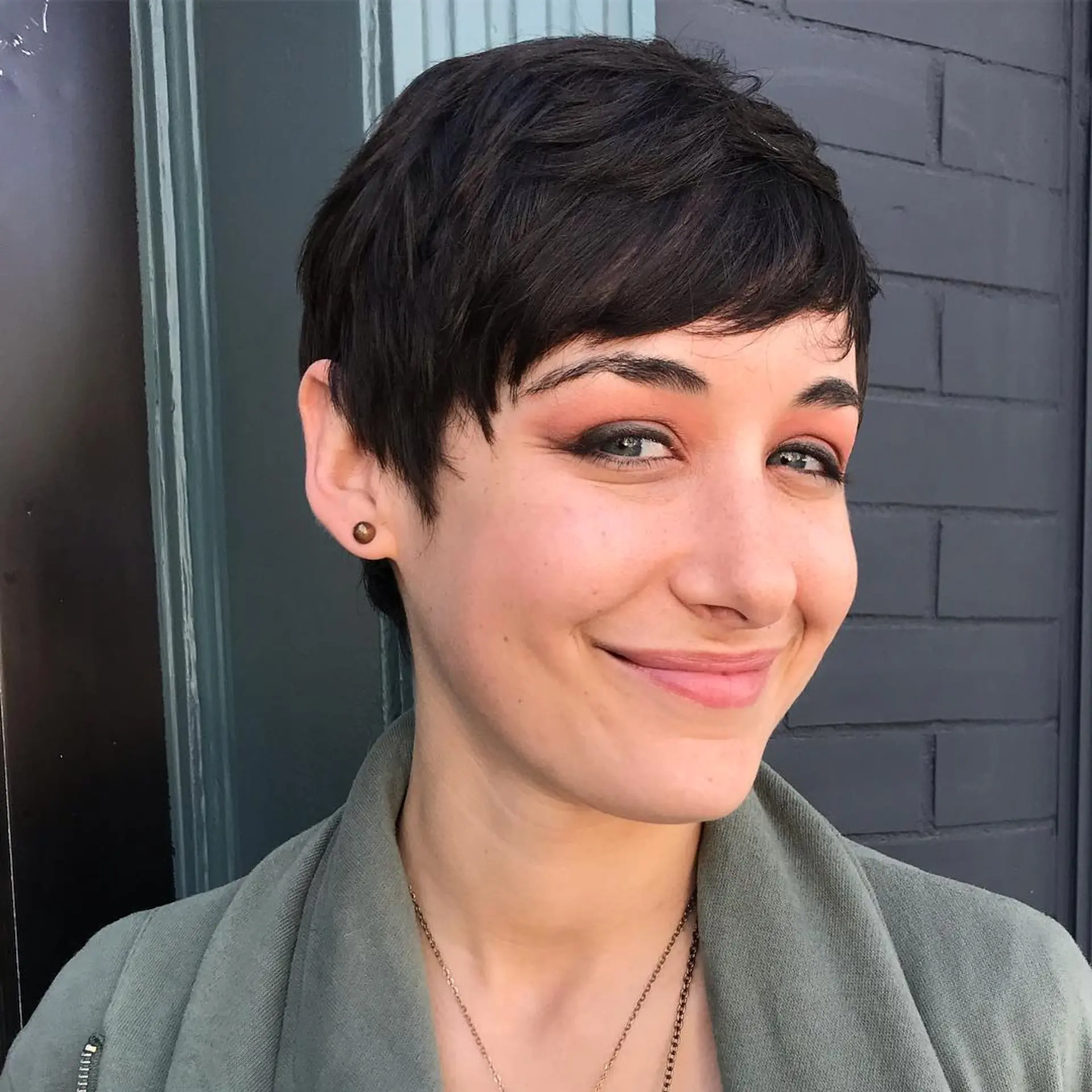 A chic, short dark brunette pixie cut with soft textured layers and subtle side-swept micro bangs framing the forehead. 1