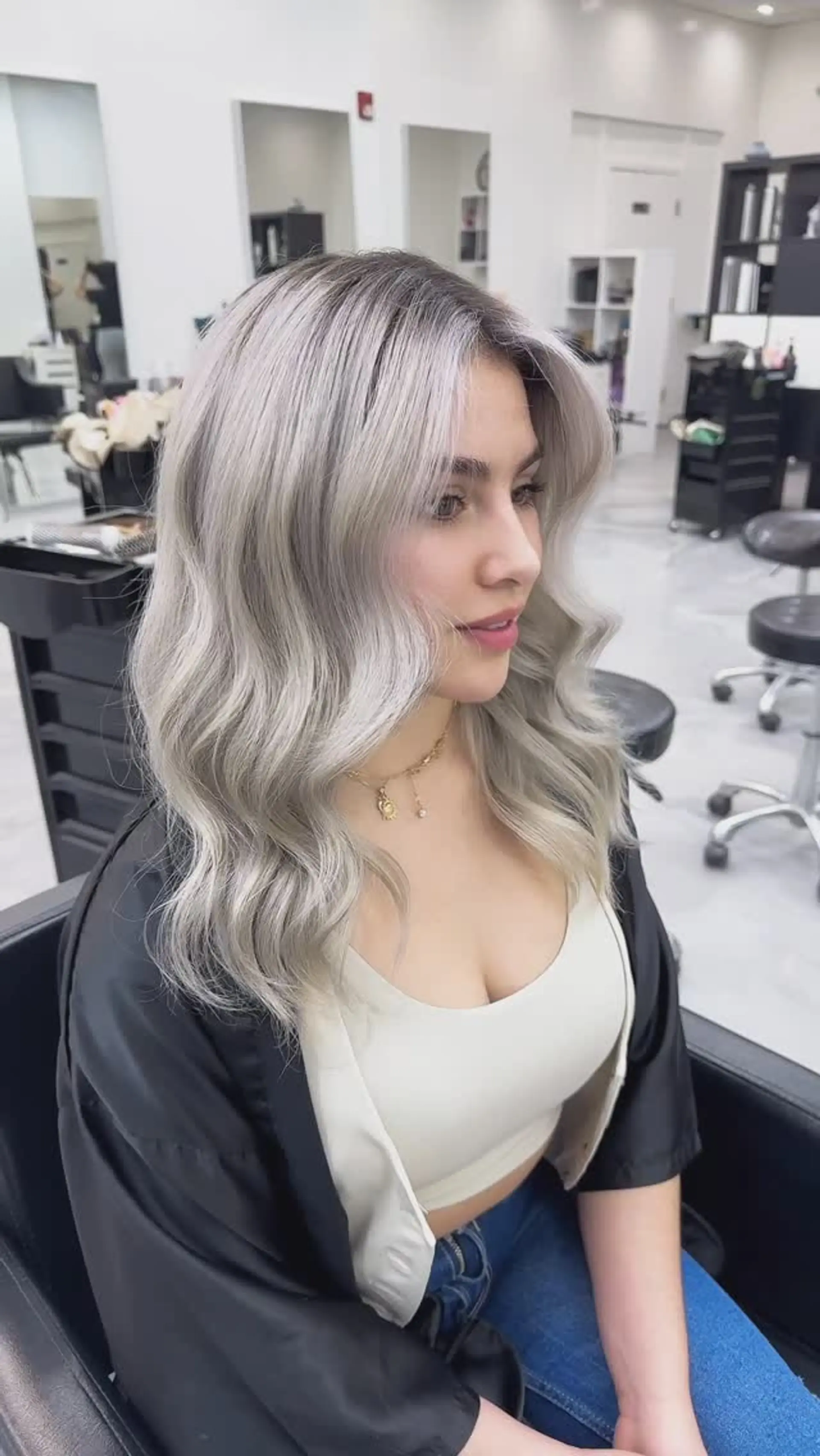 Medium-length ash blonde hair styled with loose, polished waves and a soft root shadow. 1