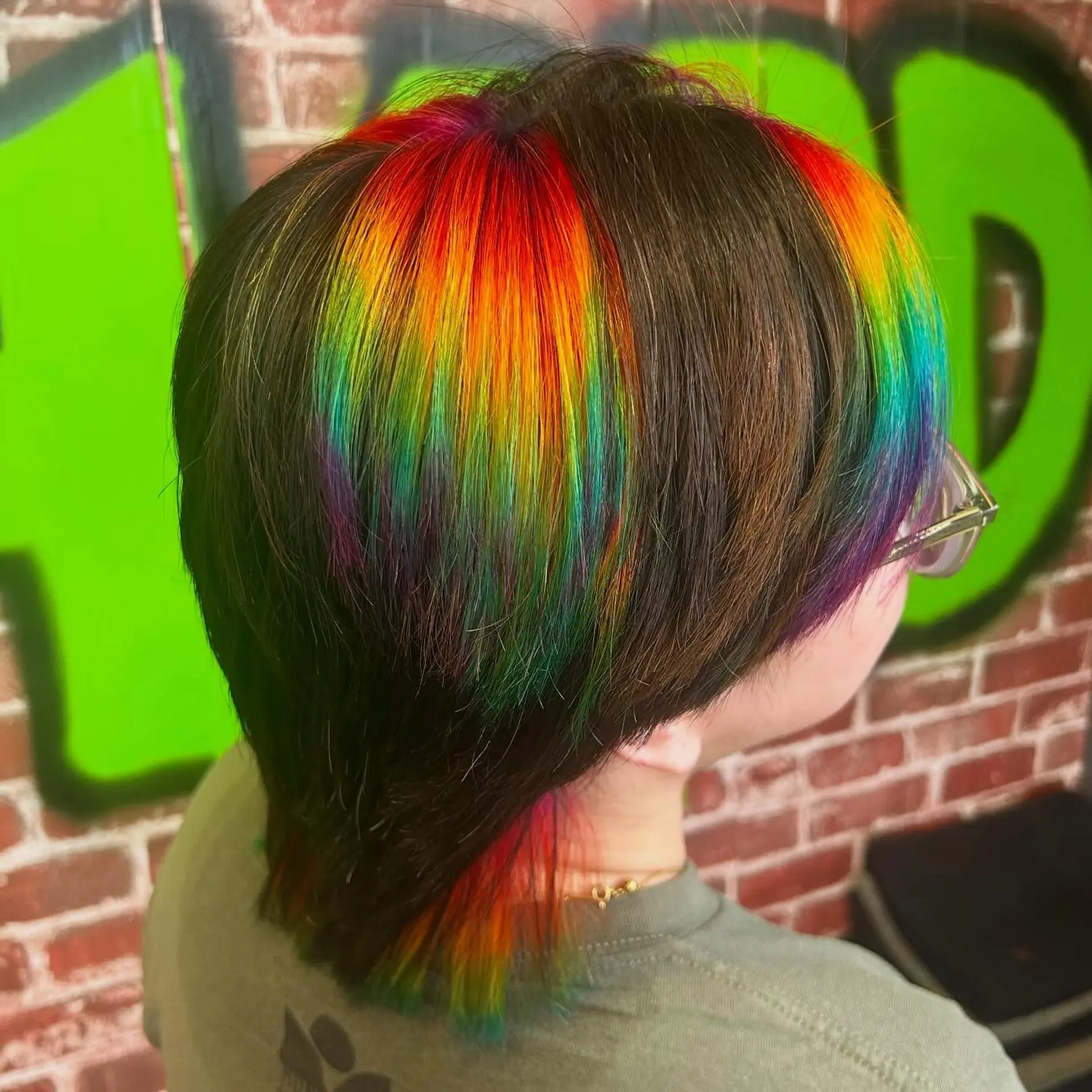 A short textured mullet haircut featuring a bold, chunky rainbow prism highlight panel against a dark brown base. 1