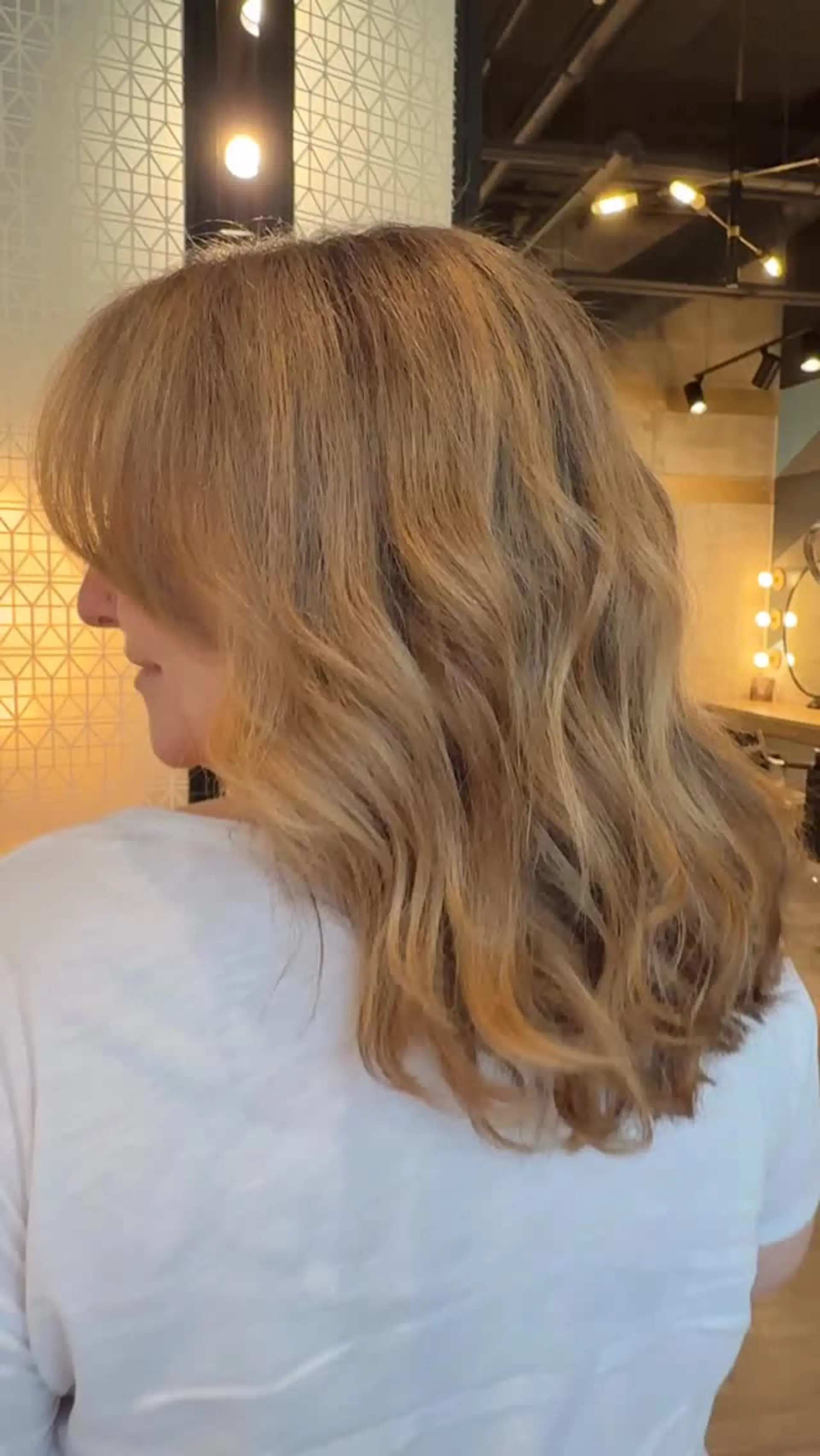 Shoulder-length warm blonde hair with blended highlights, styled in soft waves with fringe. 1