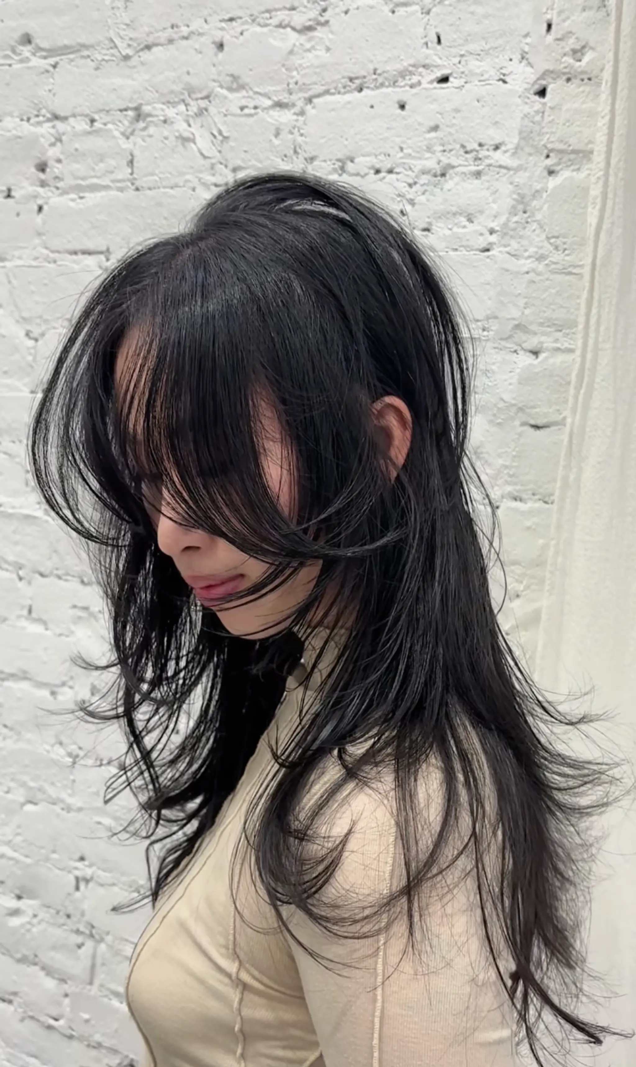 This long, jet-black wavy hairstyle includes face-framing layers and soft bangs. It has a voluminous crown and light, feathery ends, creating a mysterious and elegant appearance.