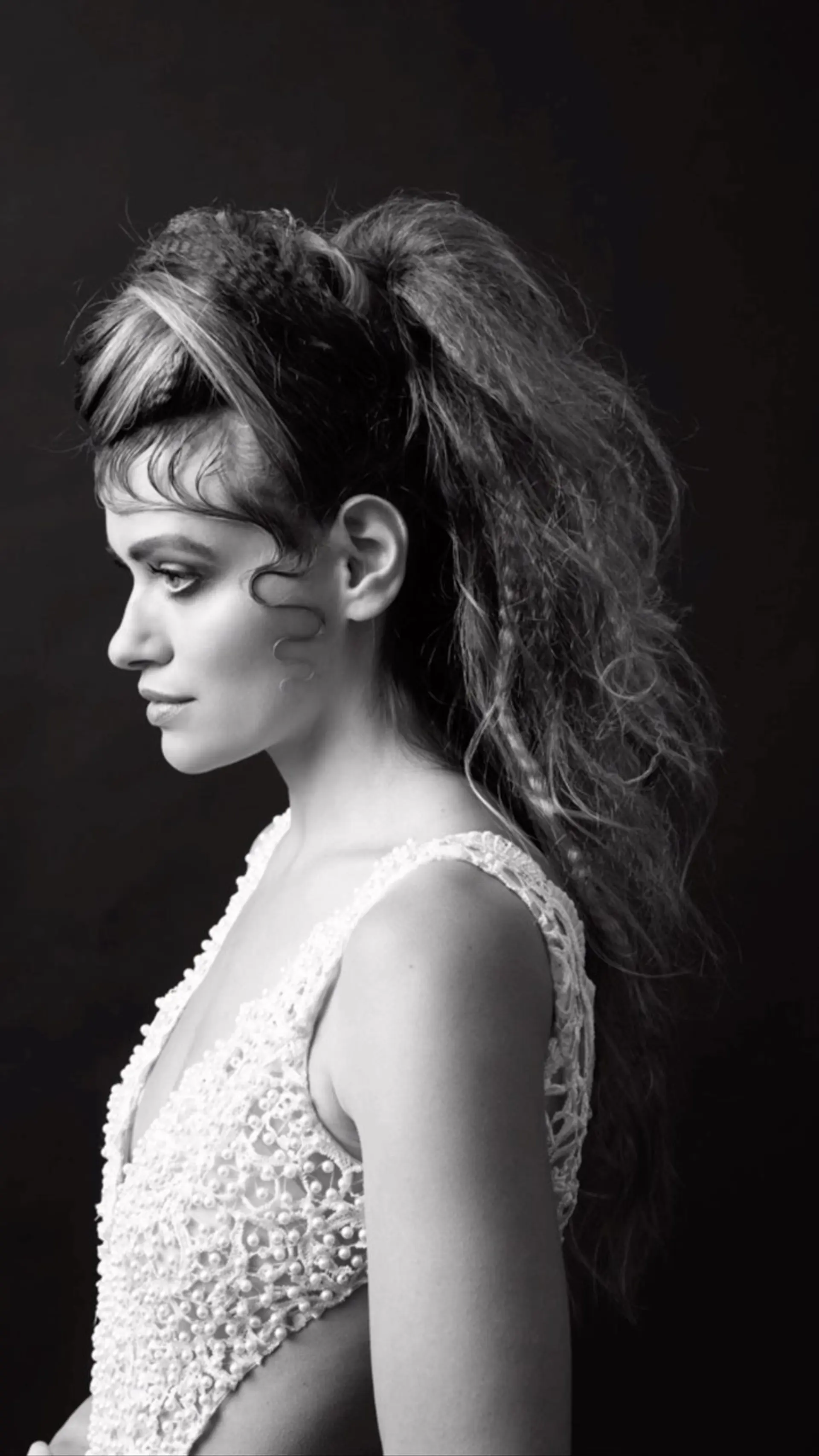 An avant-garde high ponytail styled with dramatic crimped texture throughout the back and sculpted, retro finger waves along the hairline and cheek. 1