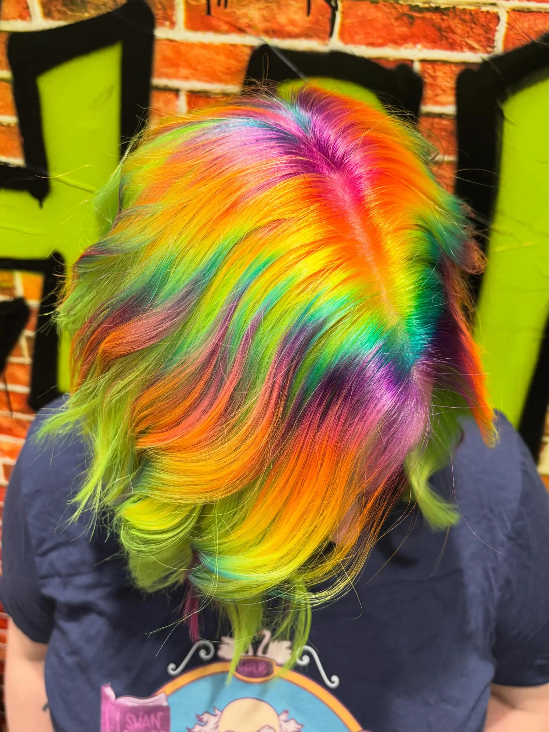 A multi-tonal rainbow vivid hair color styled with soft waves and parted smoothly to showcase vibrant panels of neon yellow, green, orange, magenta, and blue. 1