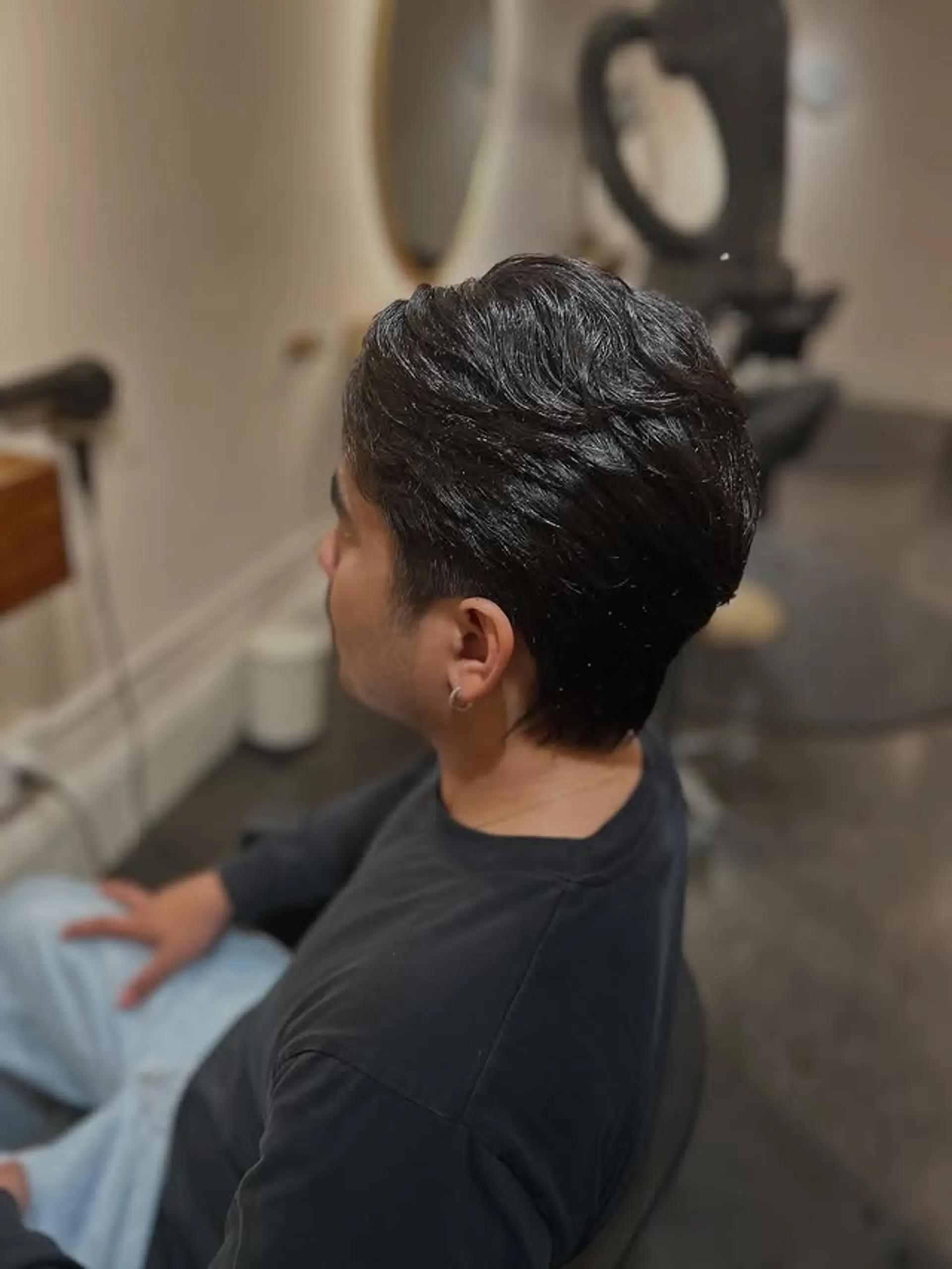 A textured, wavy men's haircut with medium length on top, styled with natural flow and volume, complemented by neatly tapered sides and back for a clean finish. 1