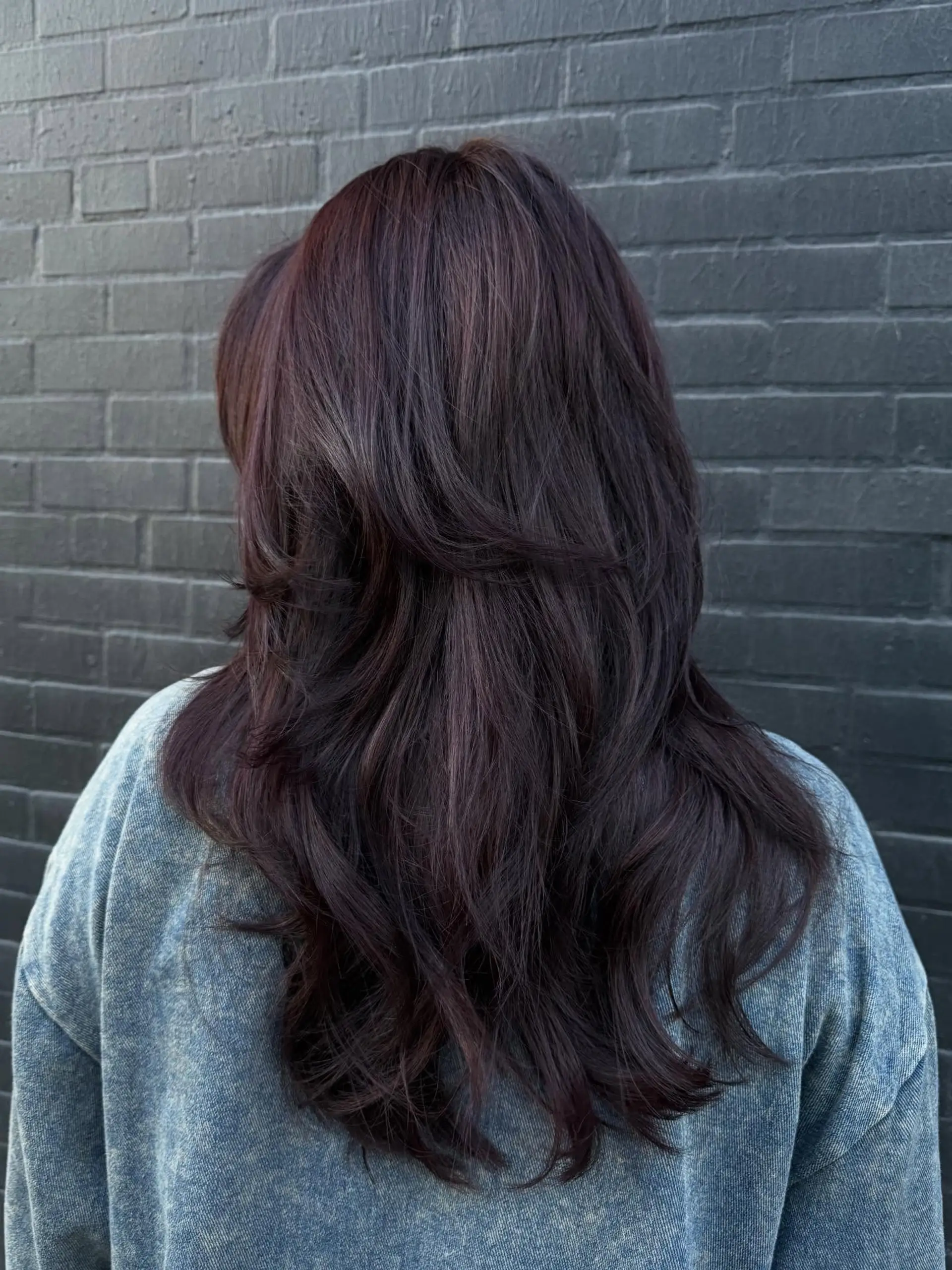 Long dark burgundy hair styled with feathered, flowing layers and soft voluminous waves. 1