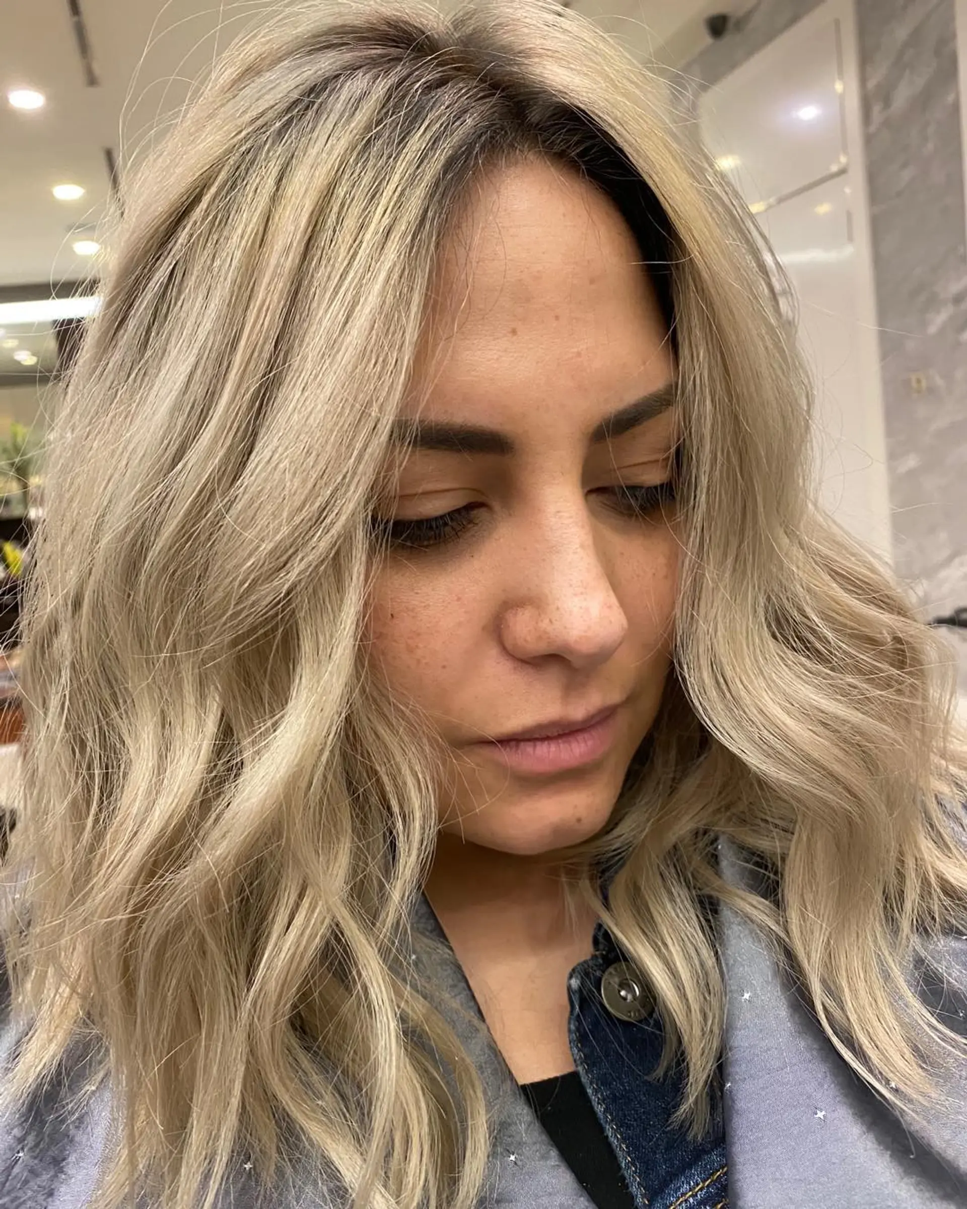 A textured medium-length lob featuring cool ash blonde balayage with a subtle shadow root, styled into soft undone waves. 1