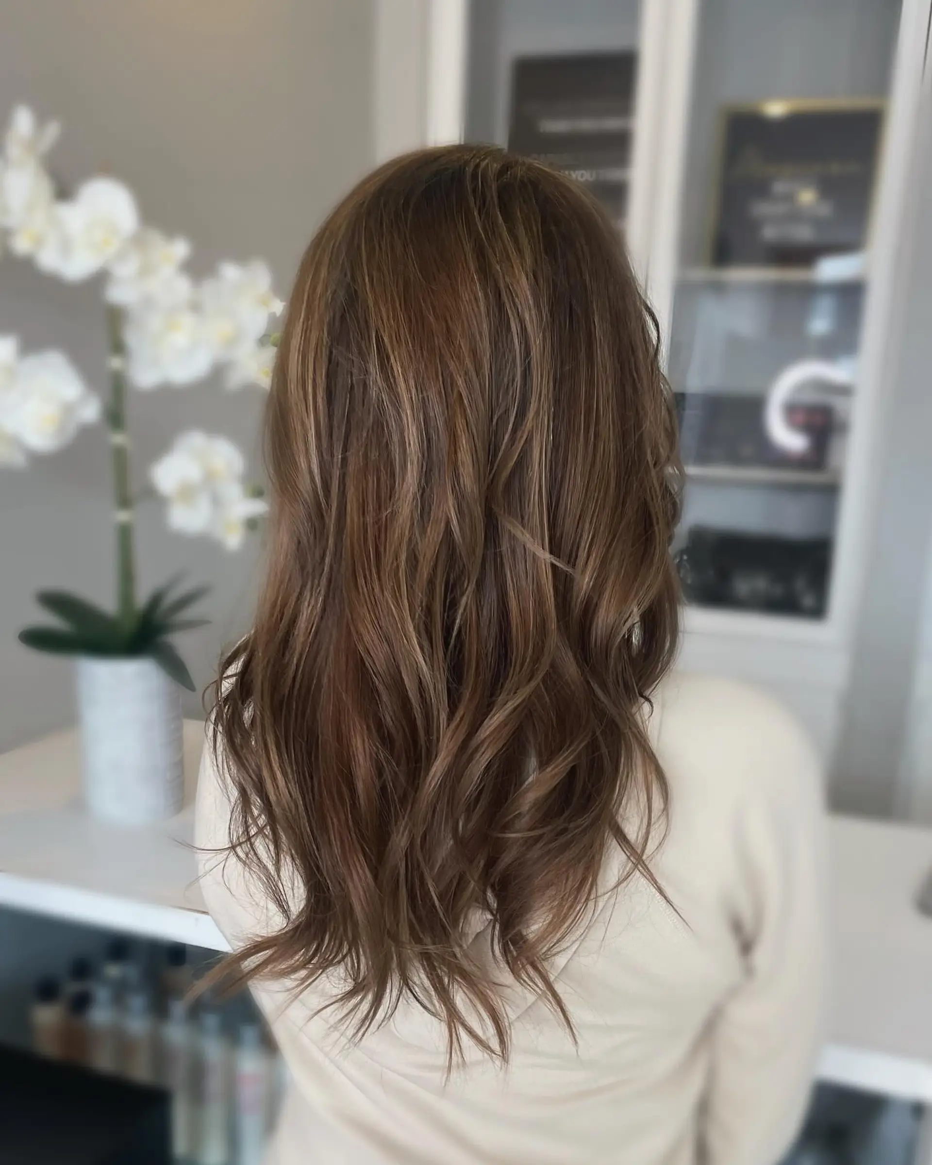 Long brown hair styled with soft, loose waves and highlighted with delicate warm caramel ribbons. 1