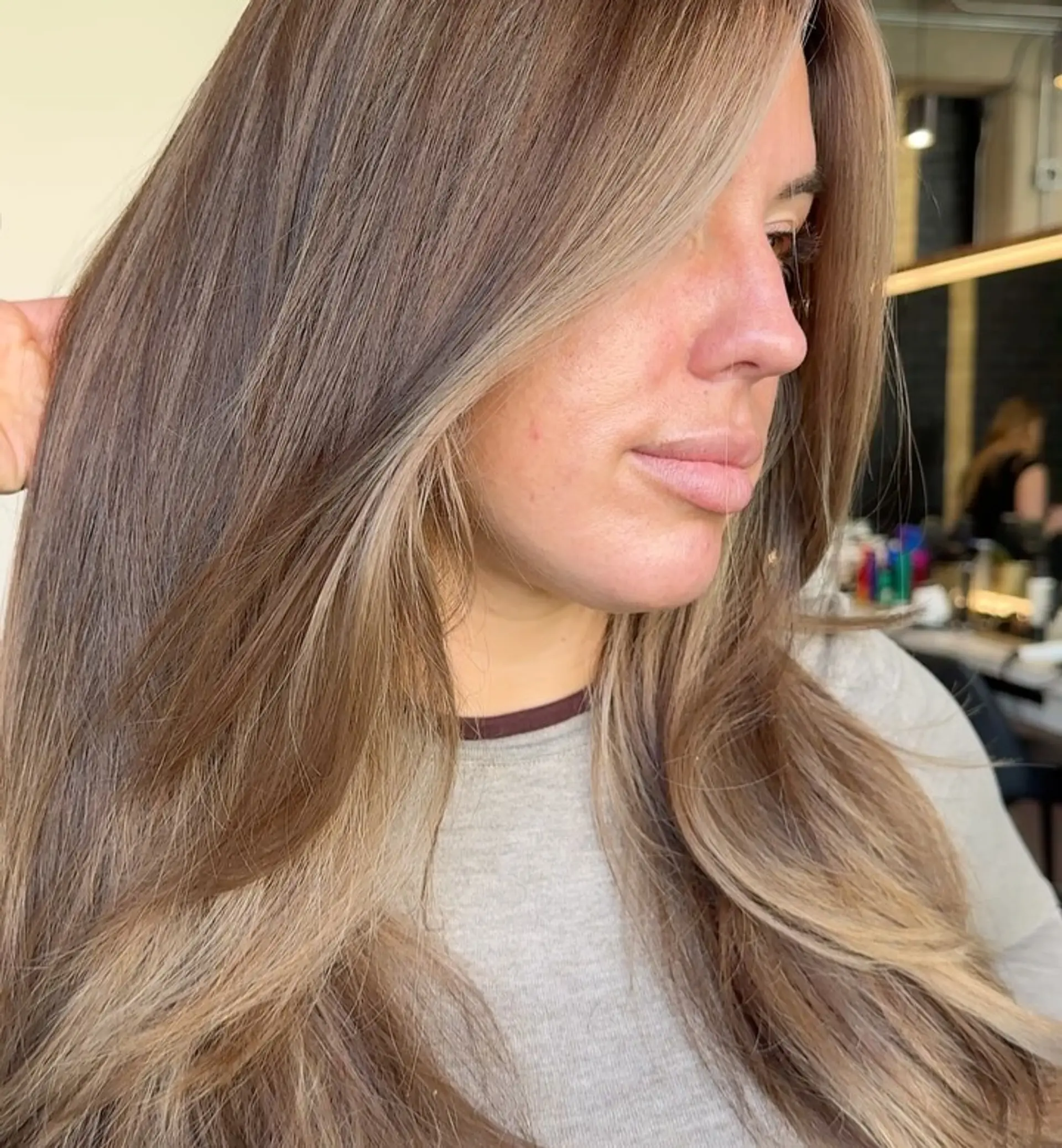 Long, flowing dimensional brunette hair with lighter caramel and ash-blonde money-piece highlights and softly layered face-framing strands. 1