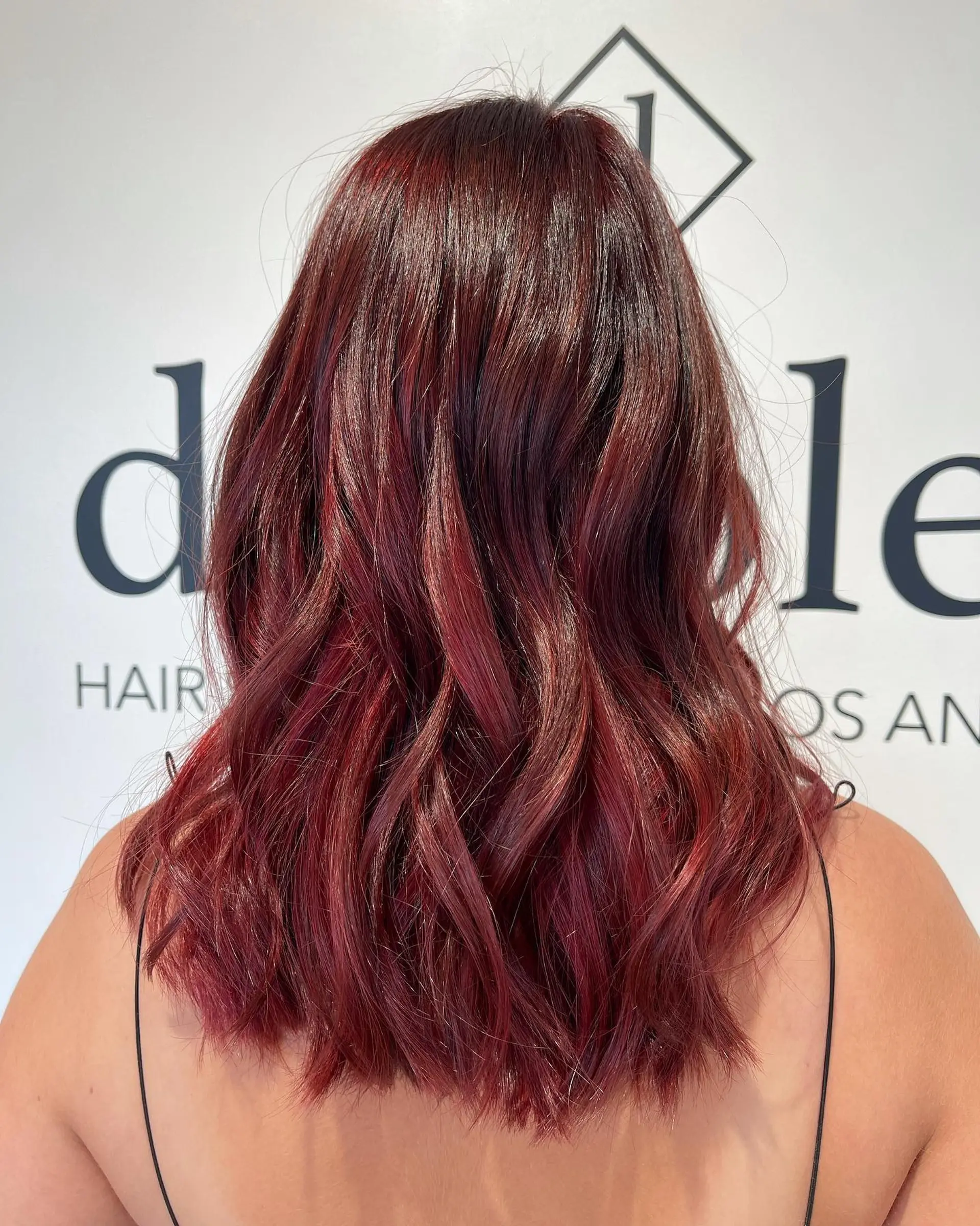 A medium-length textured lob colored in a rich, glossy burgundy-red tone with loose, defined waves throughout. 1