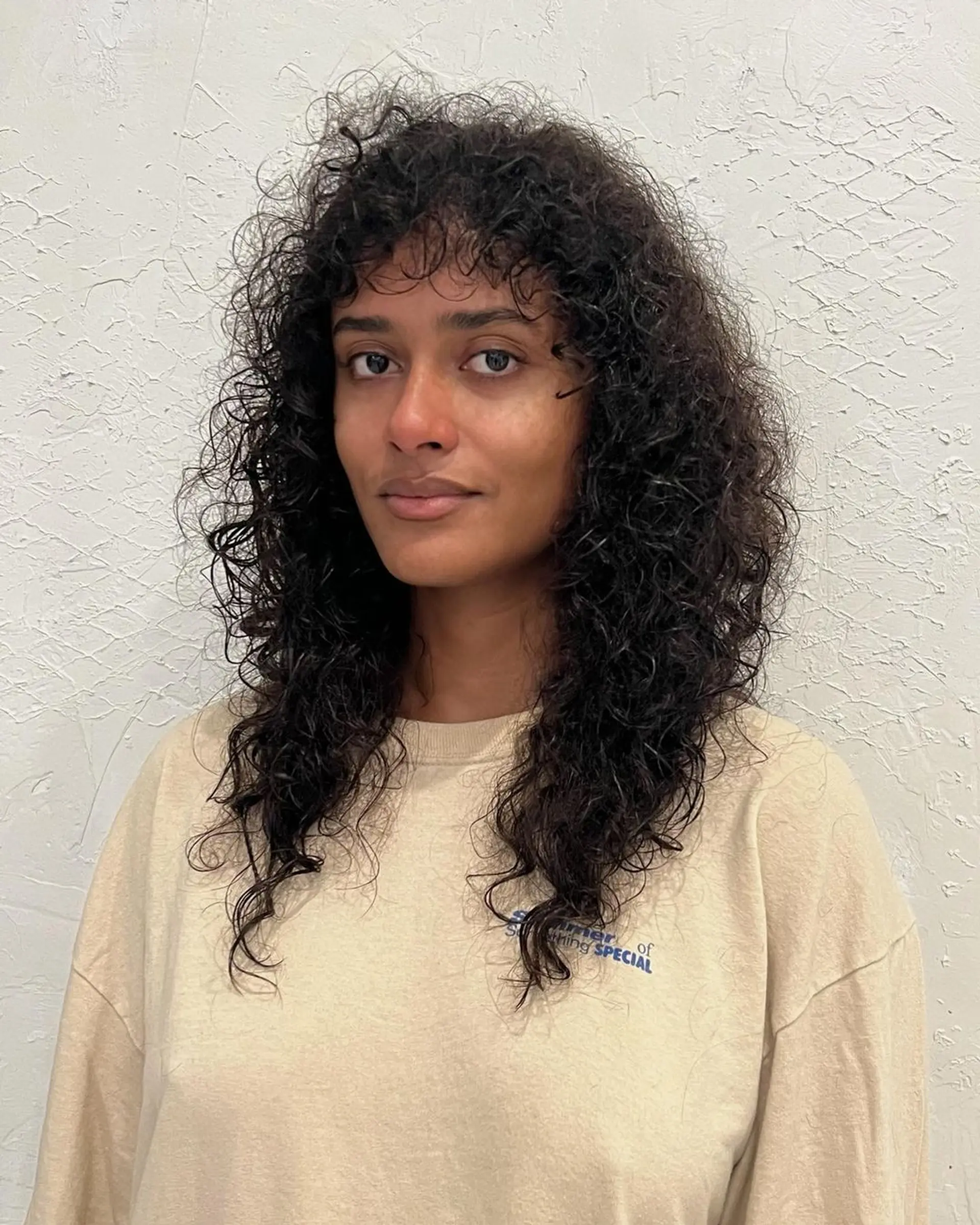 Natural curly hair with layered cuts for added volume and texture, cascading to a medium length in dark brown. 1