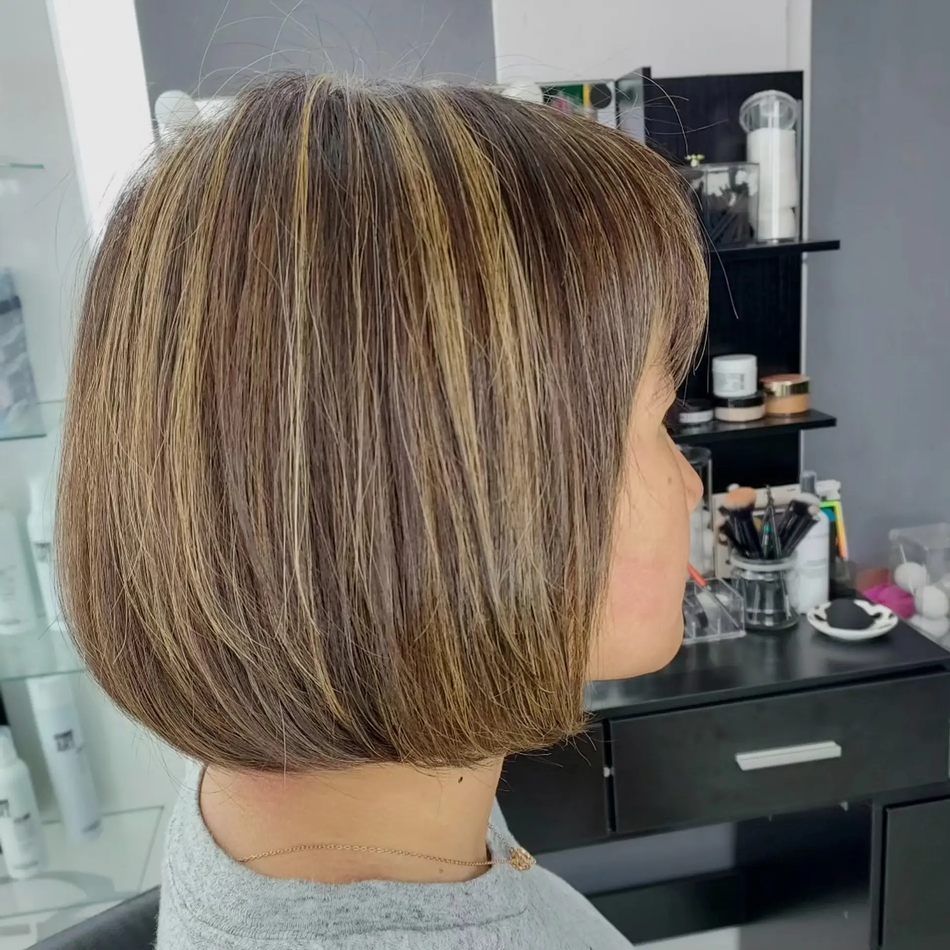 A sleek, chin-length rounded bob haircut featuring fine dimensional blonde highlights over an ash-toned base, complete with soft front fringe. 1