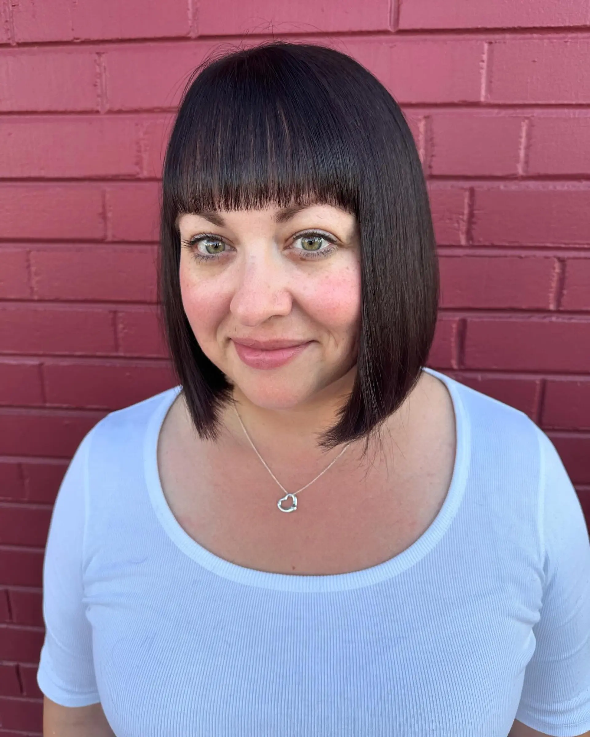 A sleek, chin-length blunt bob paired with straight-across fringe and rounded ends in a rich dark brunette shade. 1