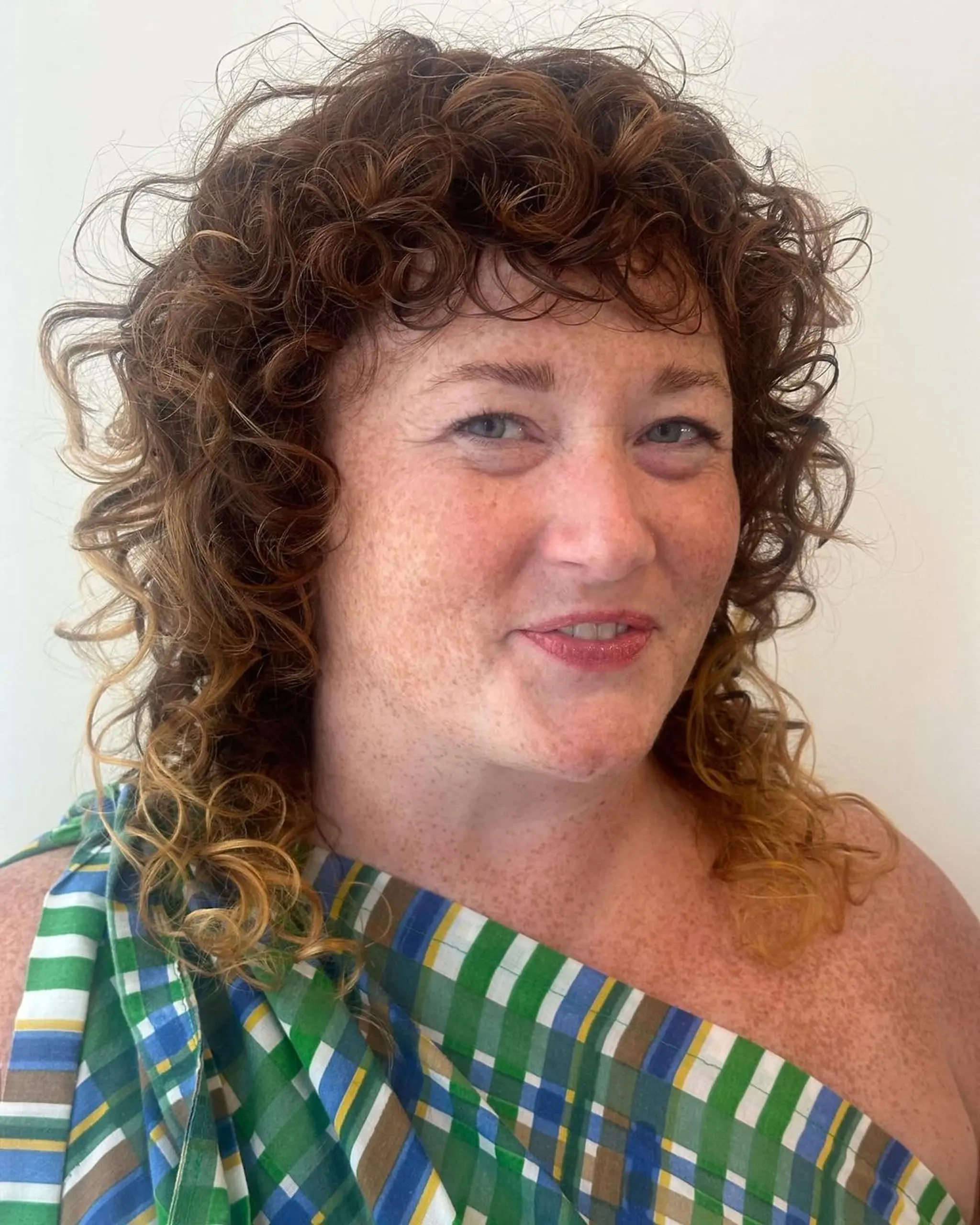 Medium-length, curly, red and blonde hairstyle featuring voluminous, layered curls with natural texture and golden highlights.
