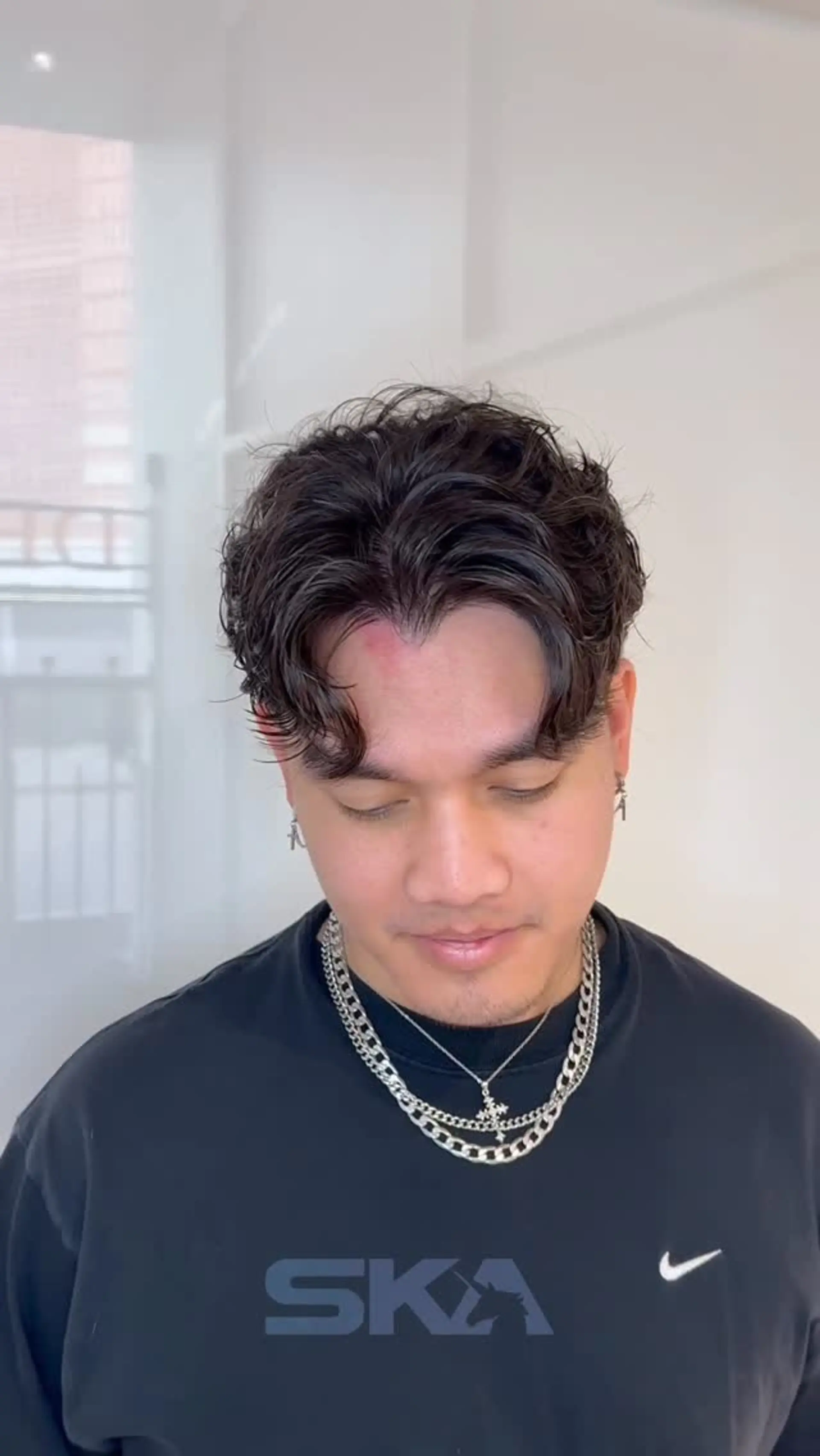 Men's short textured perm styled into soft, wavy curtain bangs with a center part. 1
