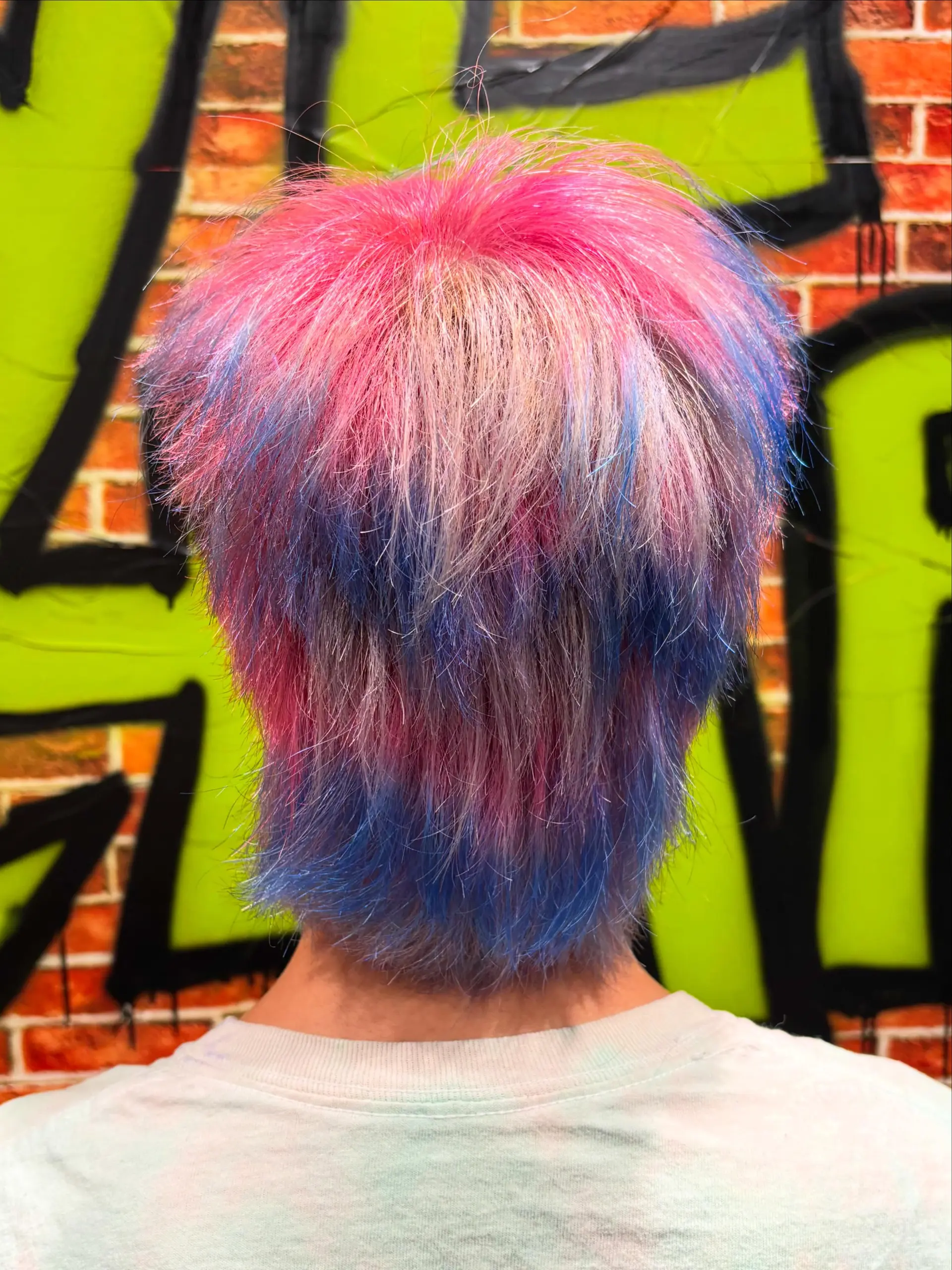 A textured short mullet featuring a creative vivid color melt transitioning from bright magenta pink at the crown into soft purple and vibrant blue at the ends. 1