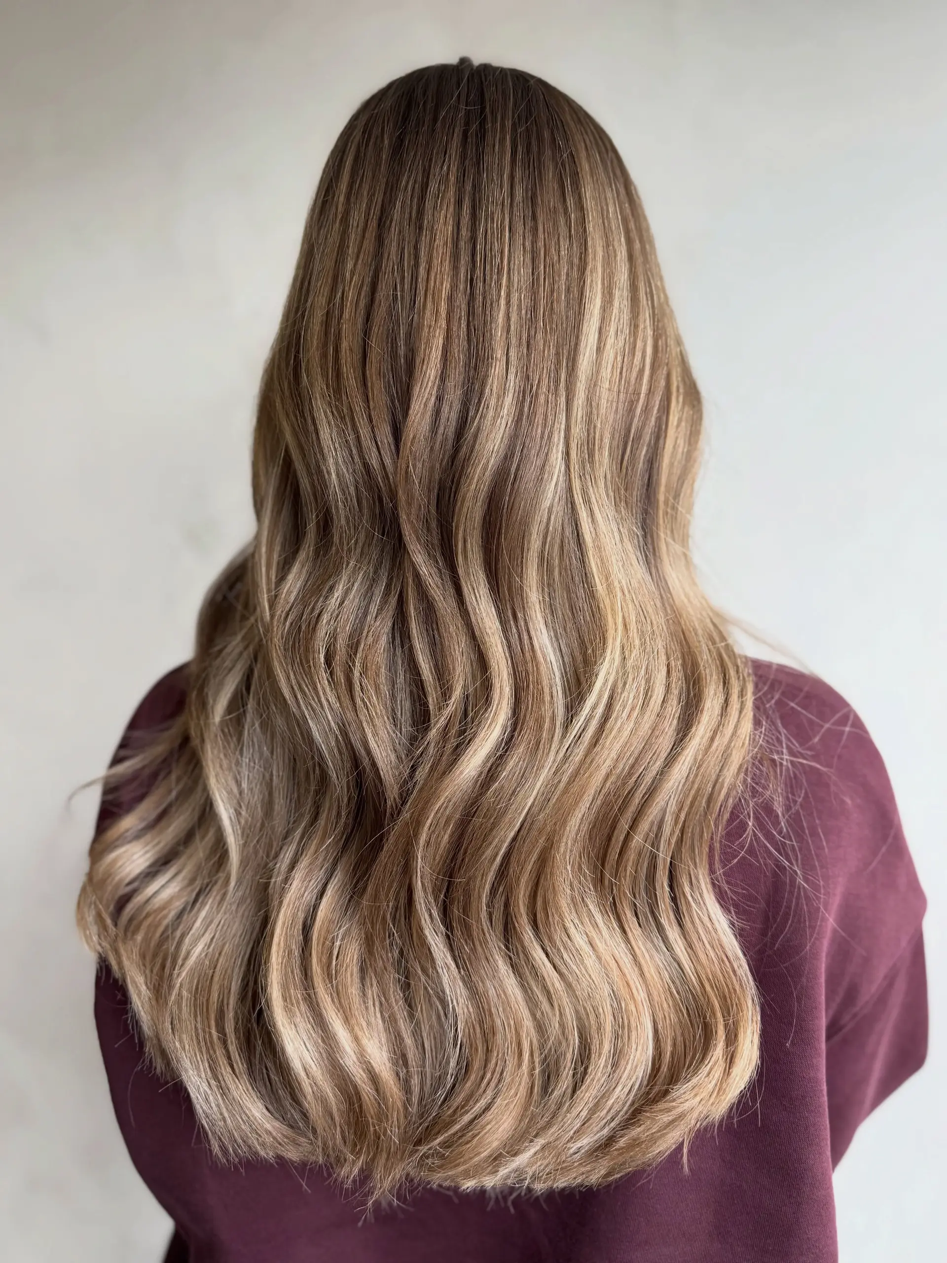 Long wavy hair featuring seamless dimensional blonde balayage highlights over a soft light brown base. 1