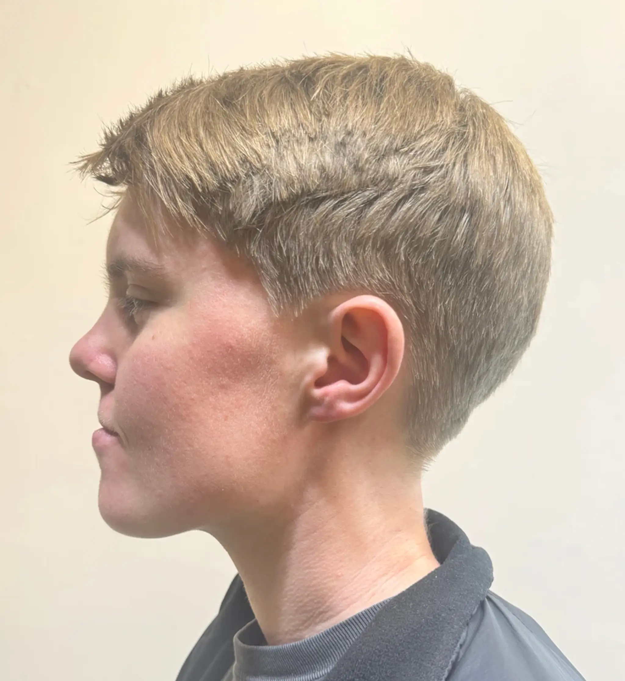 A very short, textured pixie crop with light brown, straight hair. The style is side-swept with a tapered finish, offering a refined and modern edge.