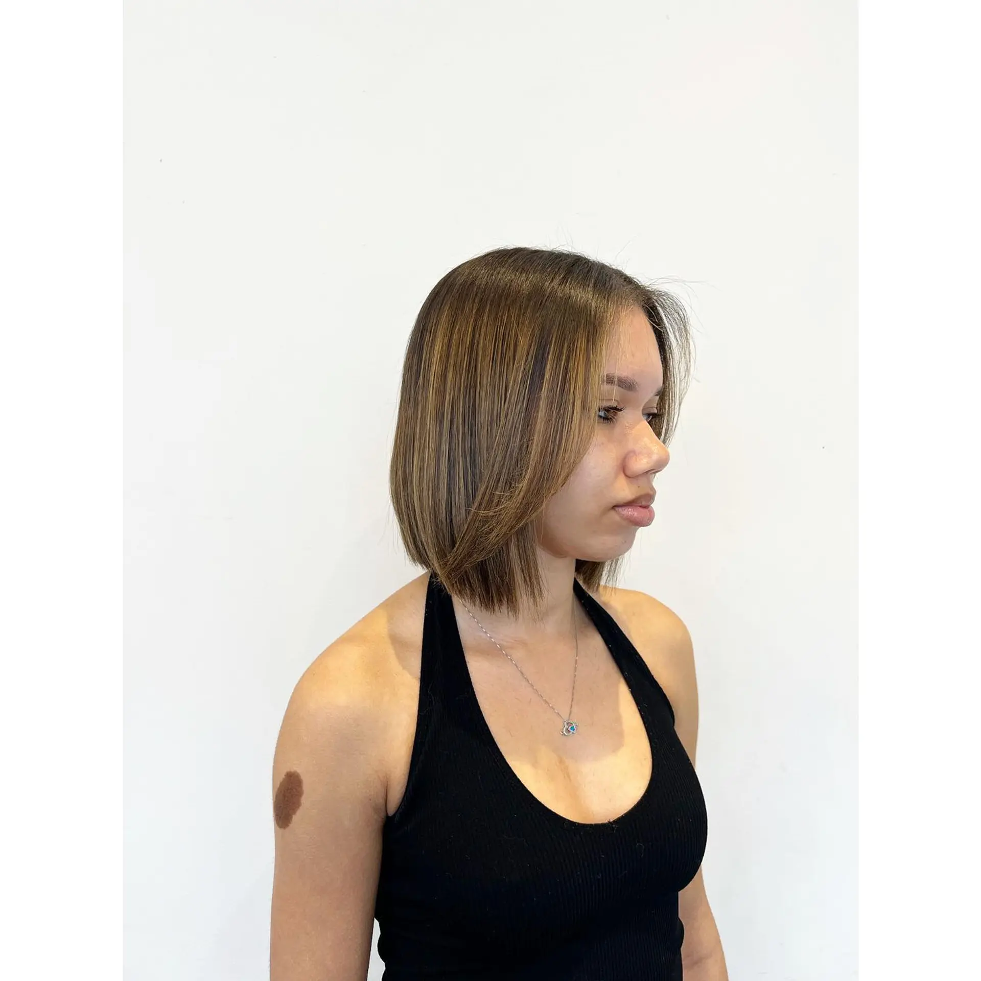 A sleek, chin-to-neck length straight bob haircut featuring fine warm honey highlights and soft face-framing layers. 1