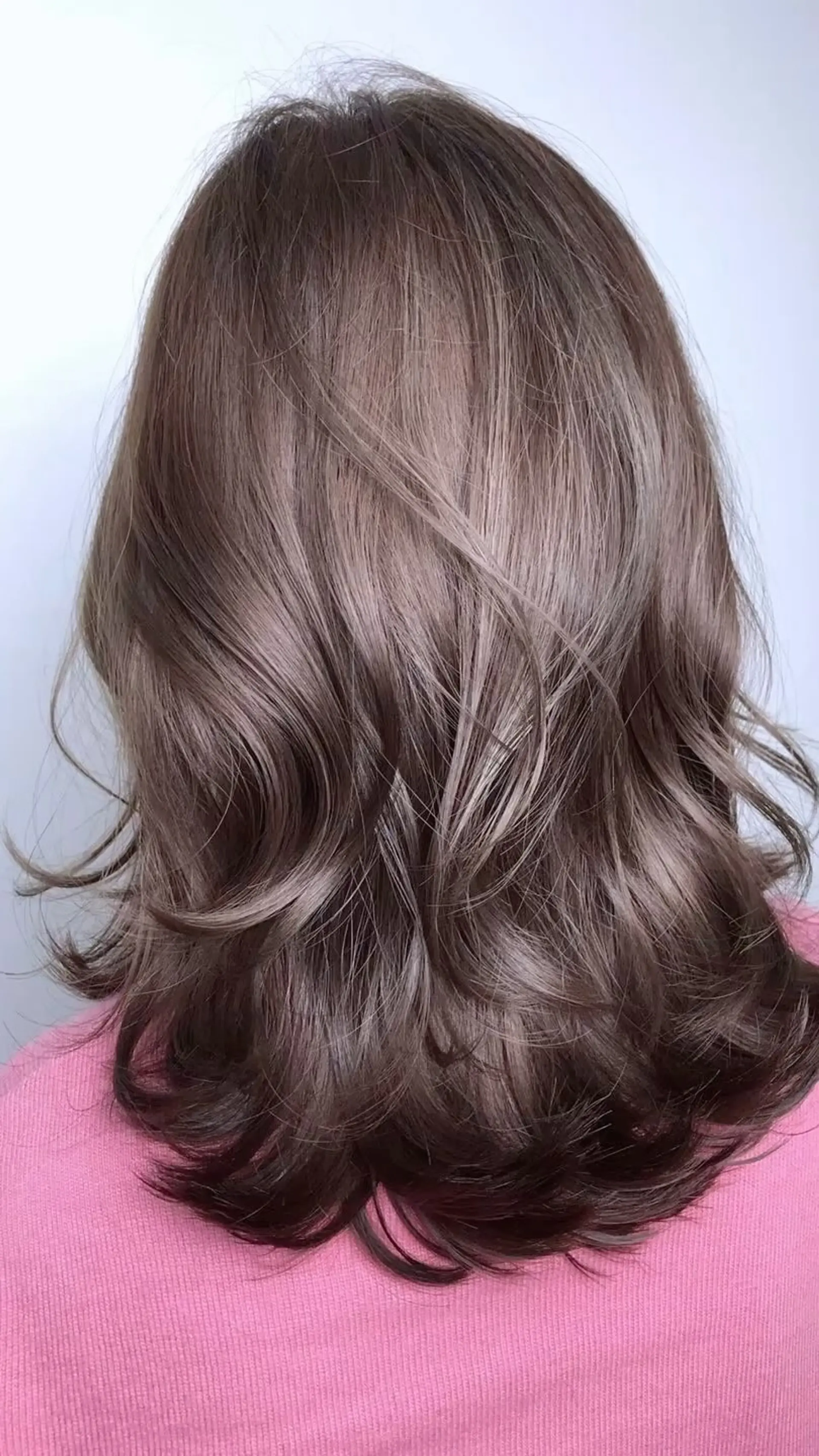 Medium-length layered haircut styled with soft textured waves in a cool ash mushroom brown hue. 1
