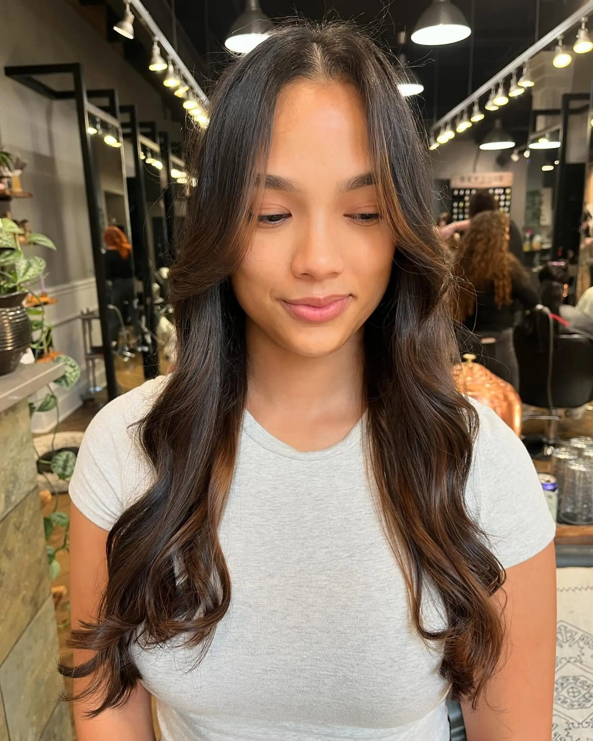 Long dark brown hair featuring subtle warm caramel balayage dimension, cut with face-framing layers and styled in soft loose waves. 1