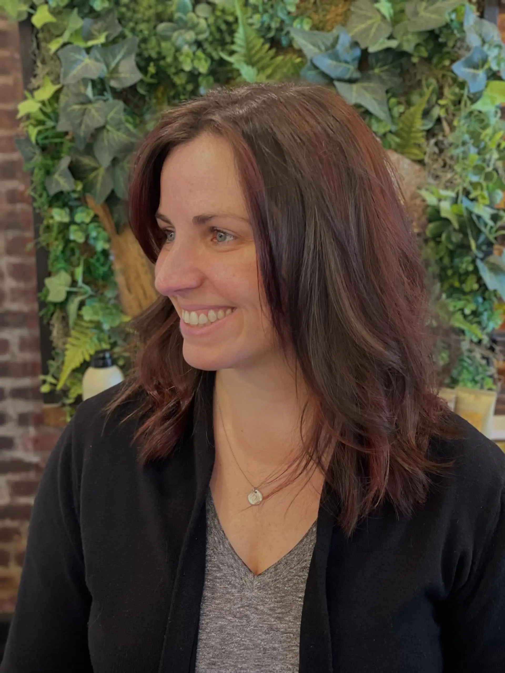 A medium-length layered cut styled with soft waves, featuring rich dark brown hair infused with warm auburn tones. Current Cut My Hair service: $215 for haircut and included finish only; displayed color is not included. 1