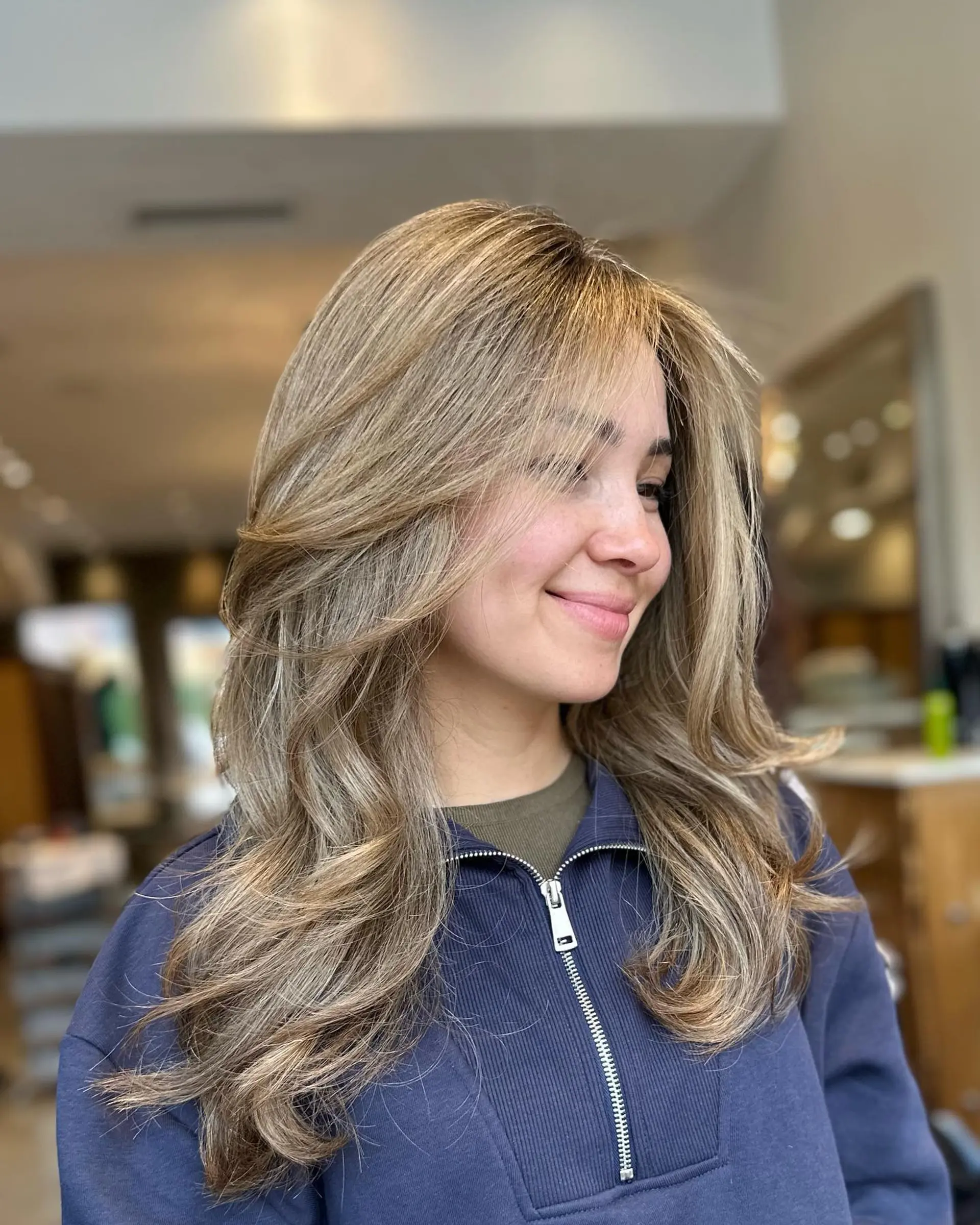 Long ash blonde and bronde hair styled with voluminous face-framing layers and soft, sweeping feathered blowout curls. 1