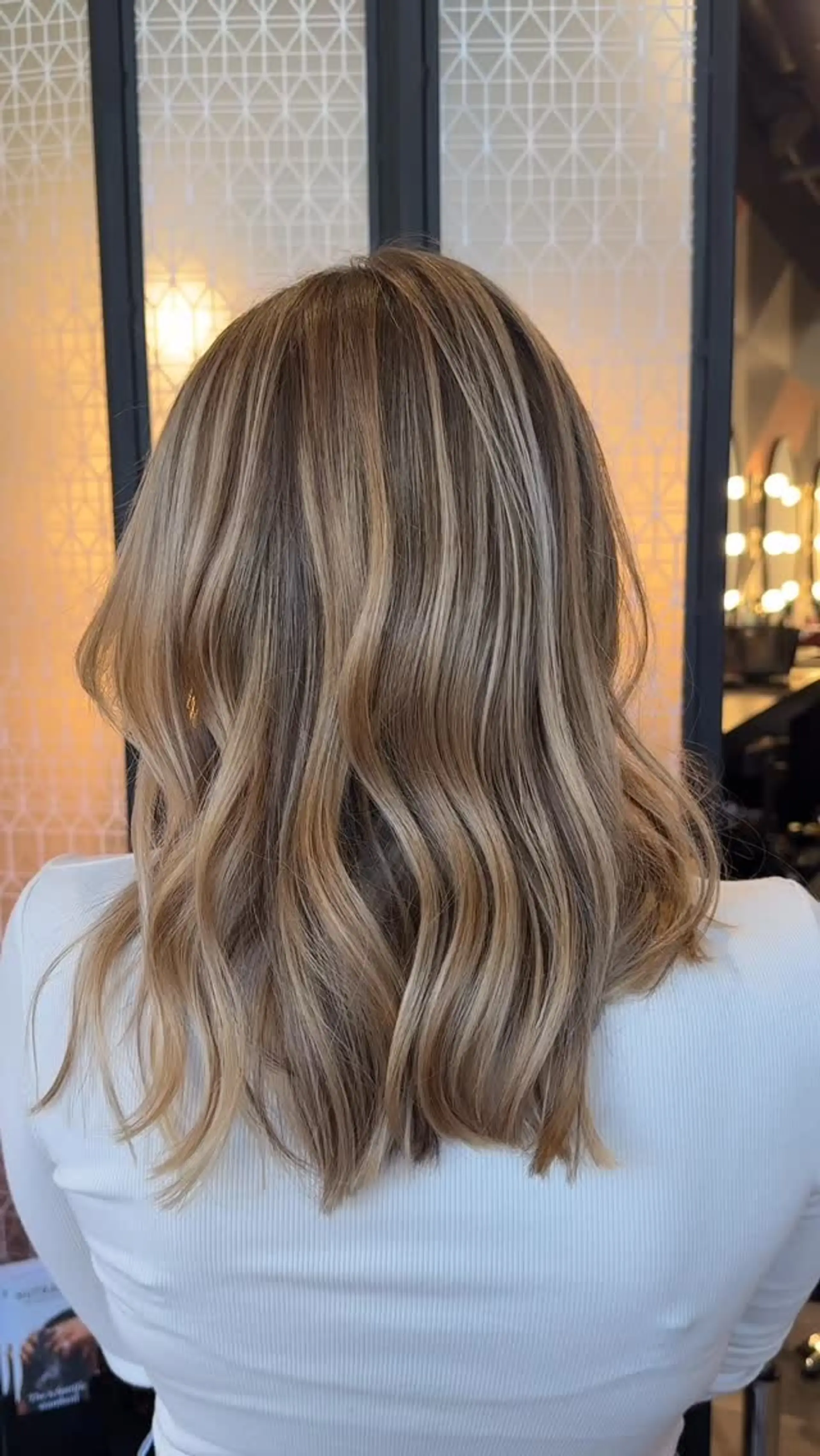 Medium-length blunt lob cut styled with soft, relaxed waves and multi-dimensional warm blonde highlights over a light brown base. 1