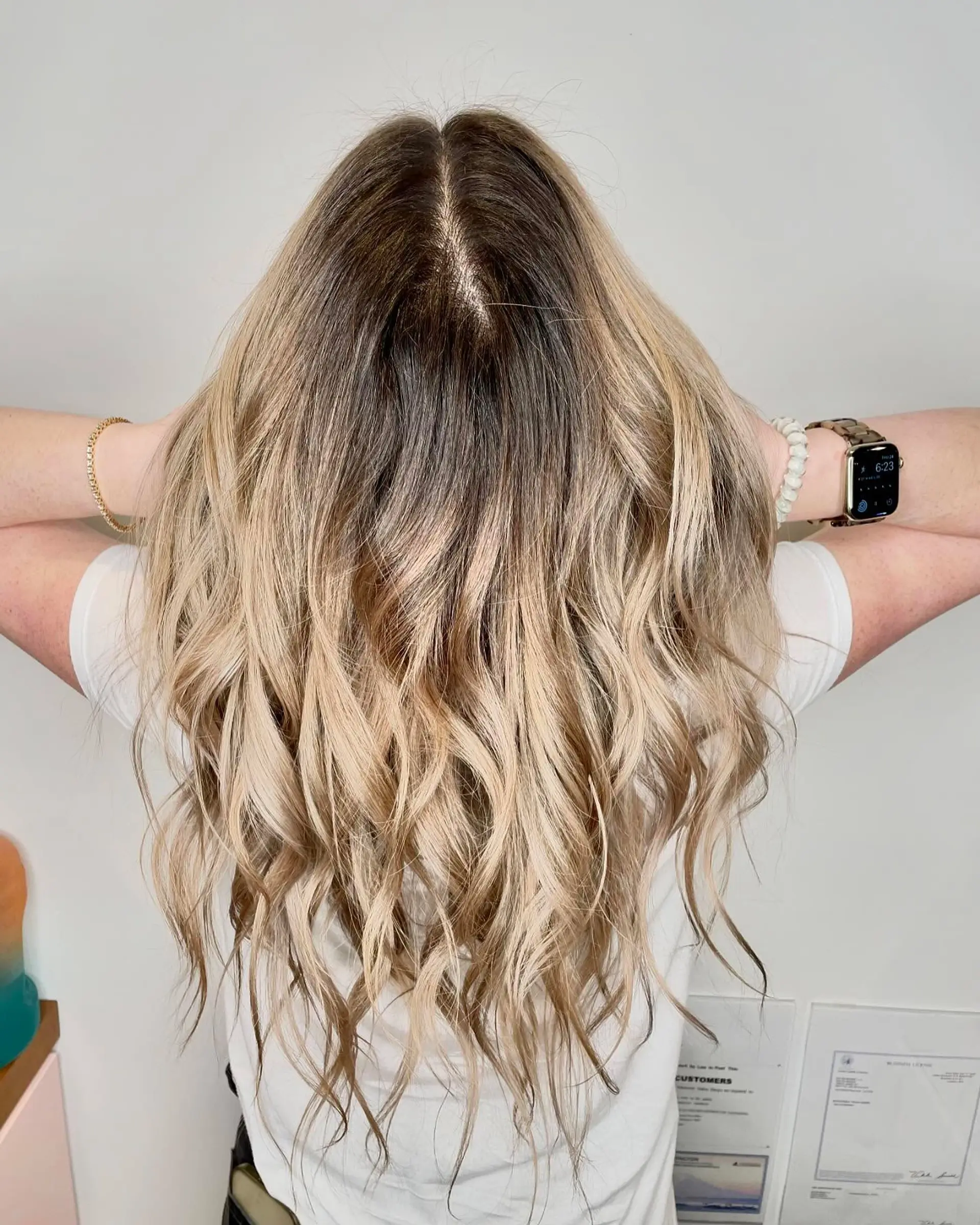 Long layered hair with a dark shadow root transitioning into dimensional mushroom ash blonde styled in textured beach waves. 1