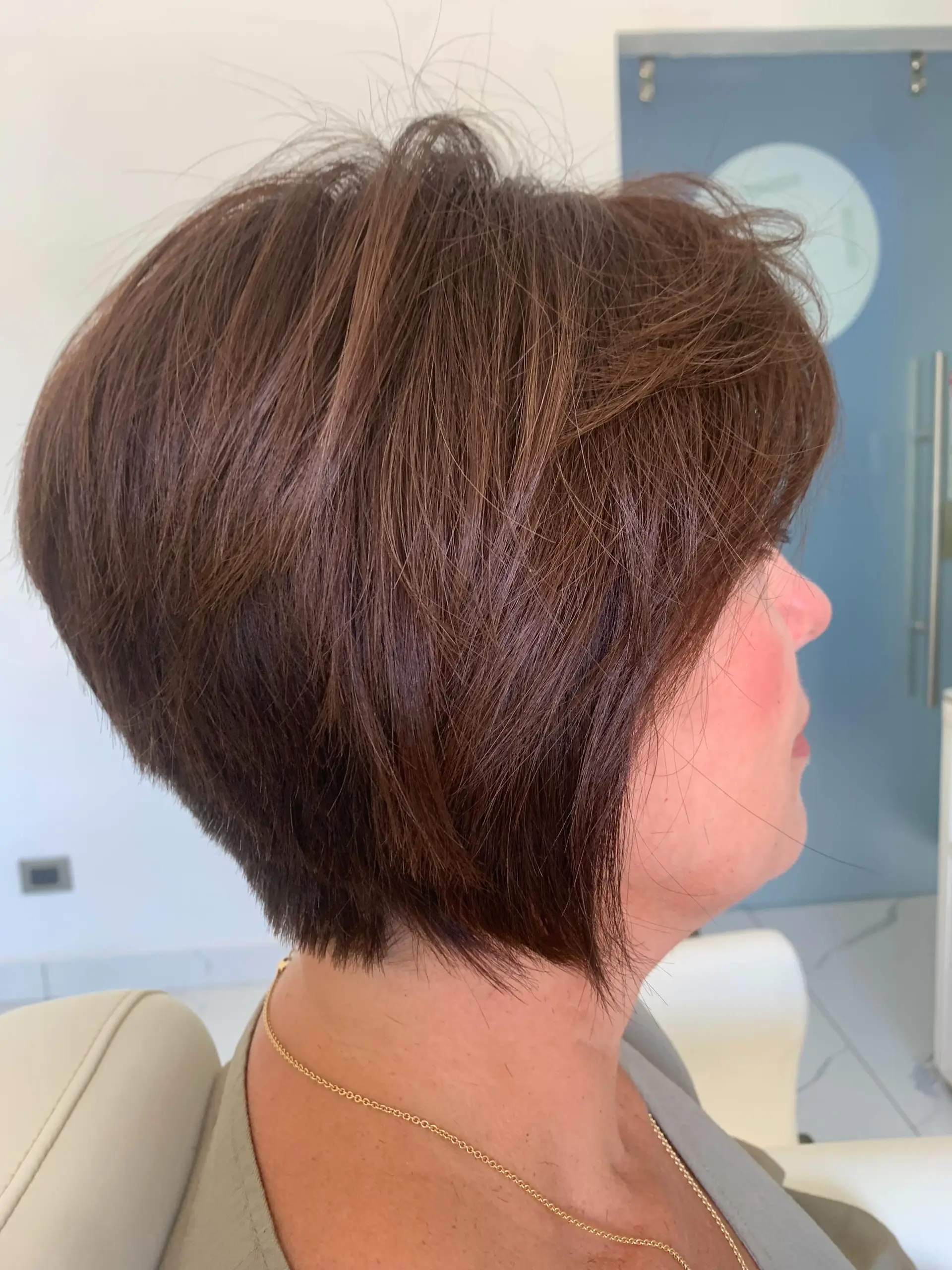A side-profile view of a layered textured short bob haircut in a warm chestnut brown shade. 1