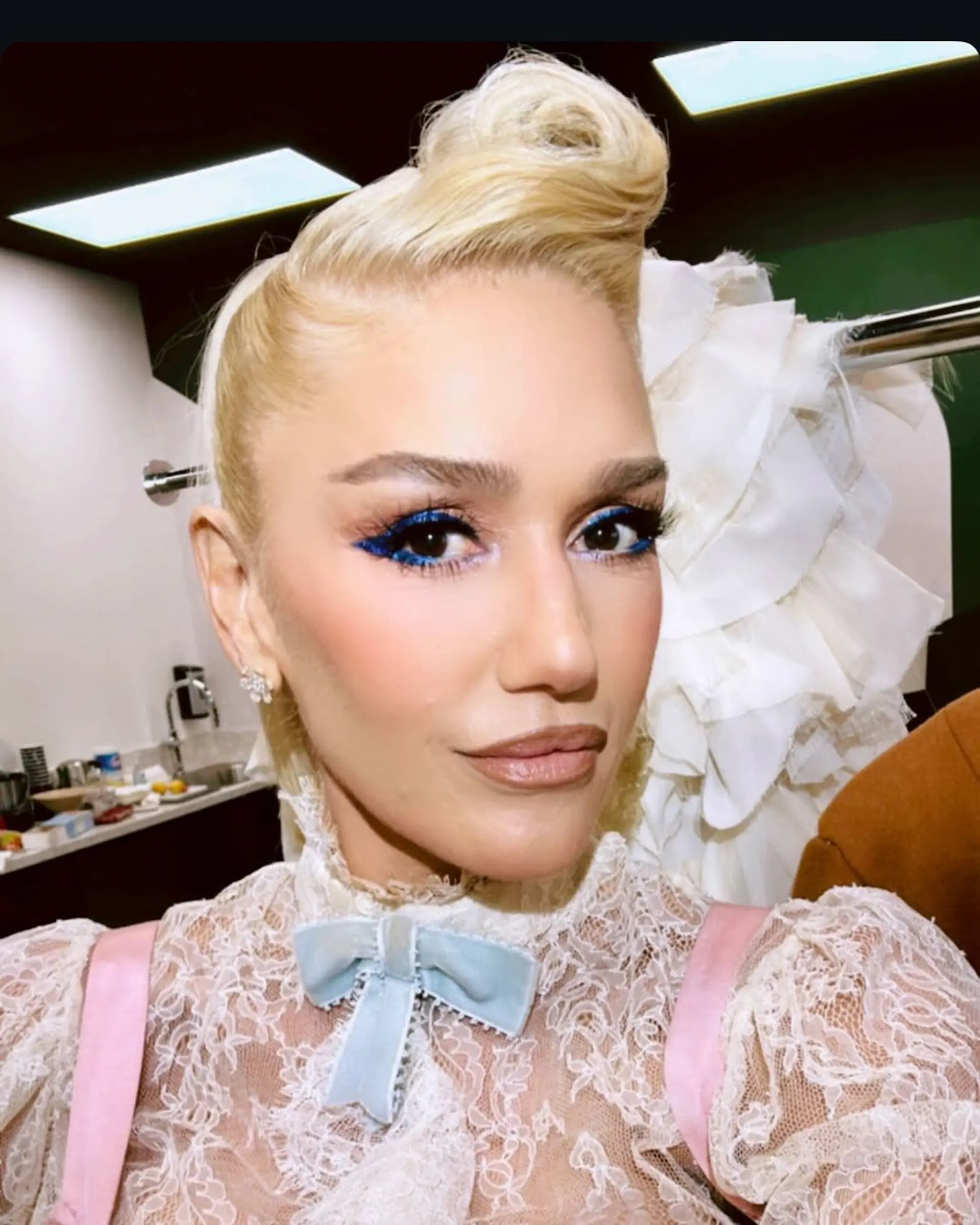 A sleek platinum blonde updo featuring a sculptured retro roll at the top crown with smooth, slicked-back sides. 1