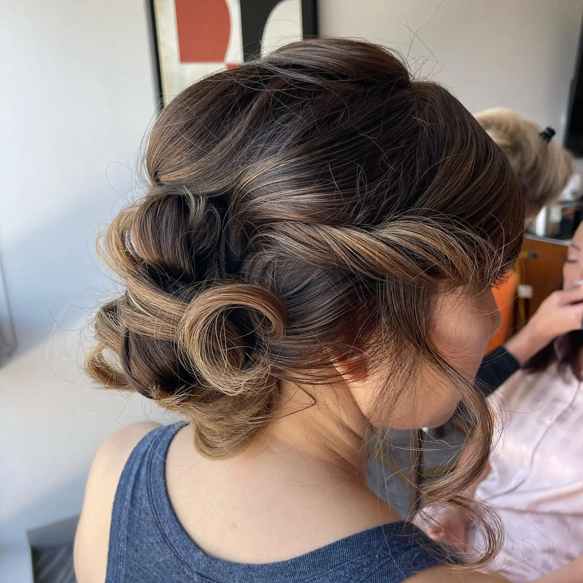 A soft, romantic low bun upstyle with voluminous texture, dimensional curls, and face-framing tendrils. 1