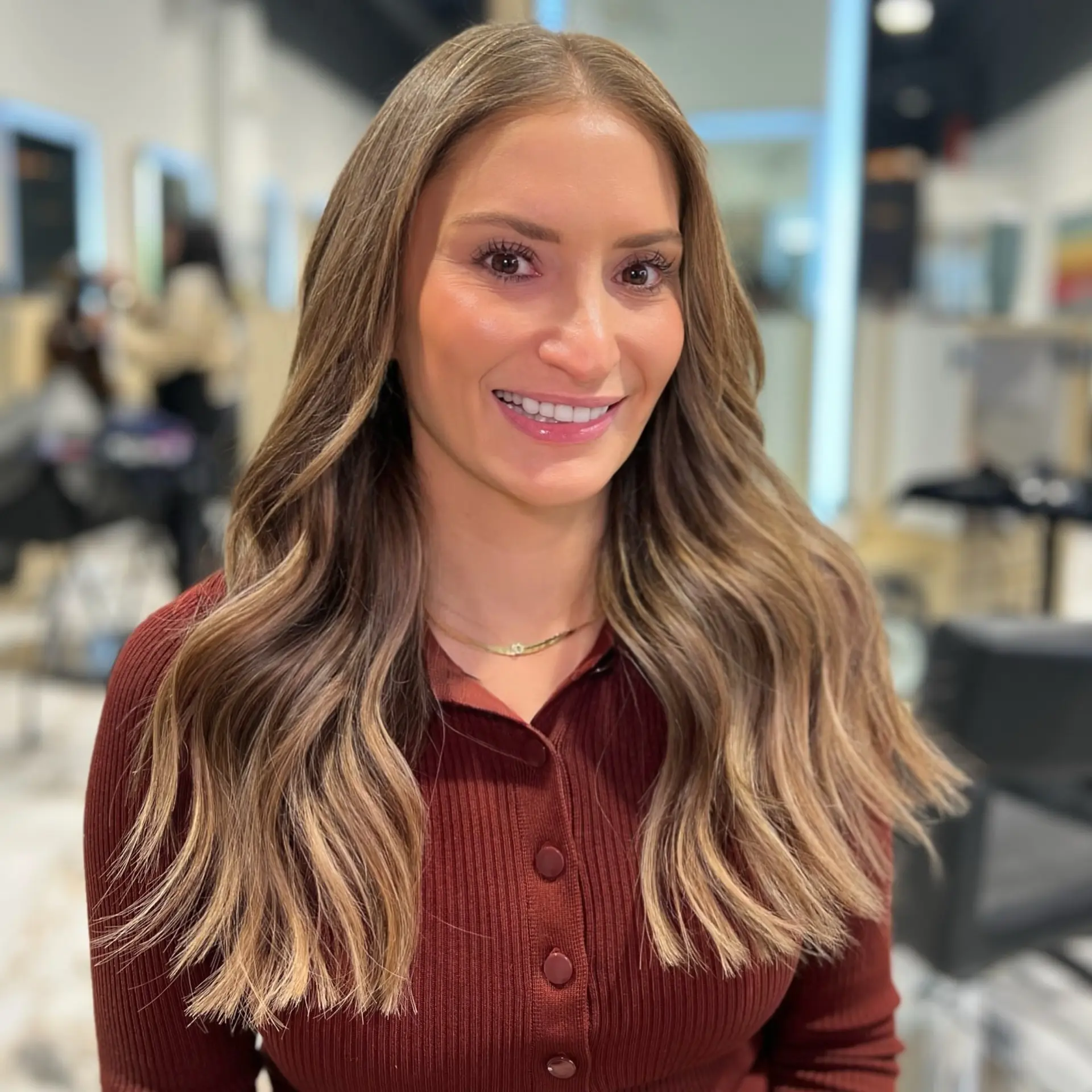 Long dimensional bronde hair styled in soft, loose waves with a center part and brightened face-framing pieces. 1