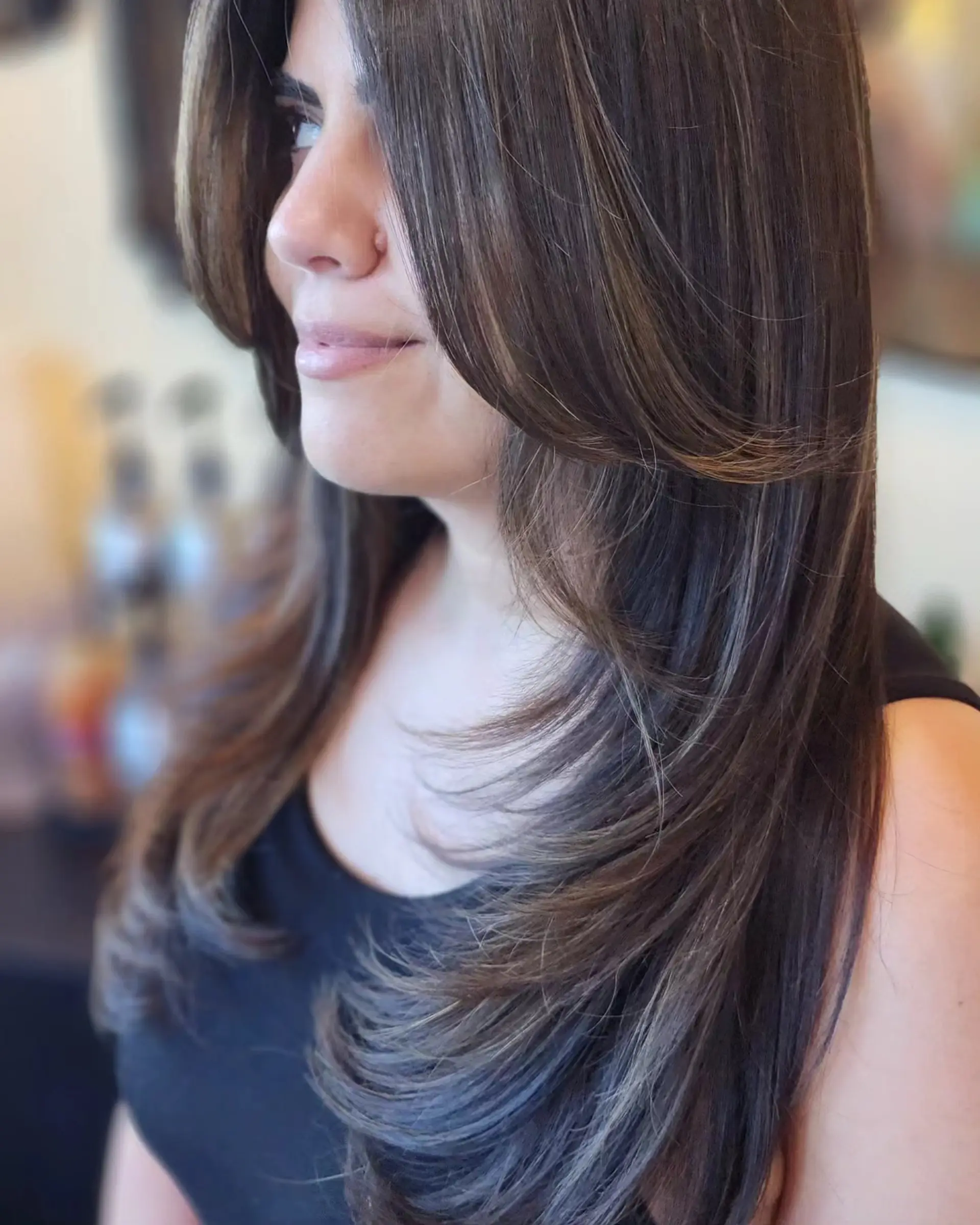 Long dark brown hair cut with soft cascading layers and face-framing curtain bangs styled into a smooth, bouncy blowout. 1