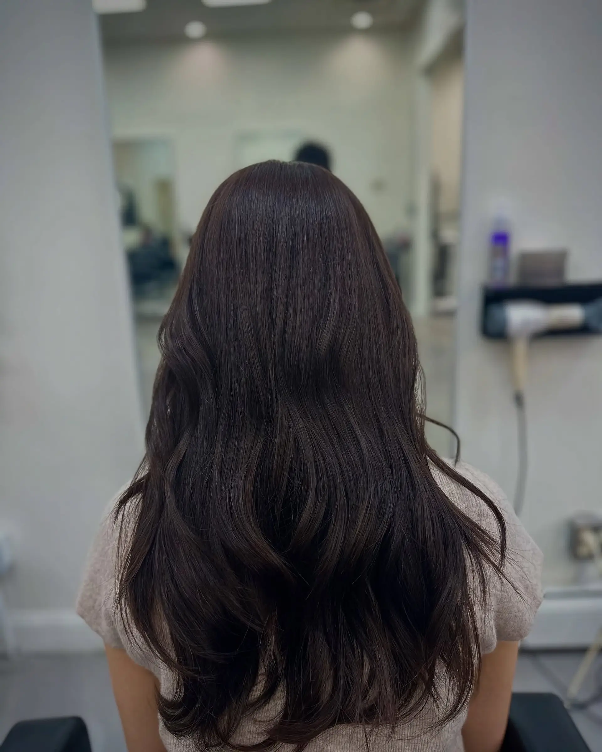 Long, glossy dark brown hair styled with soft, cascading waves and subtle layering. 1