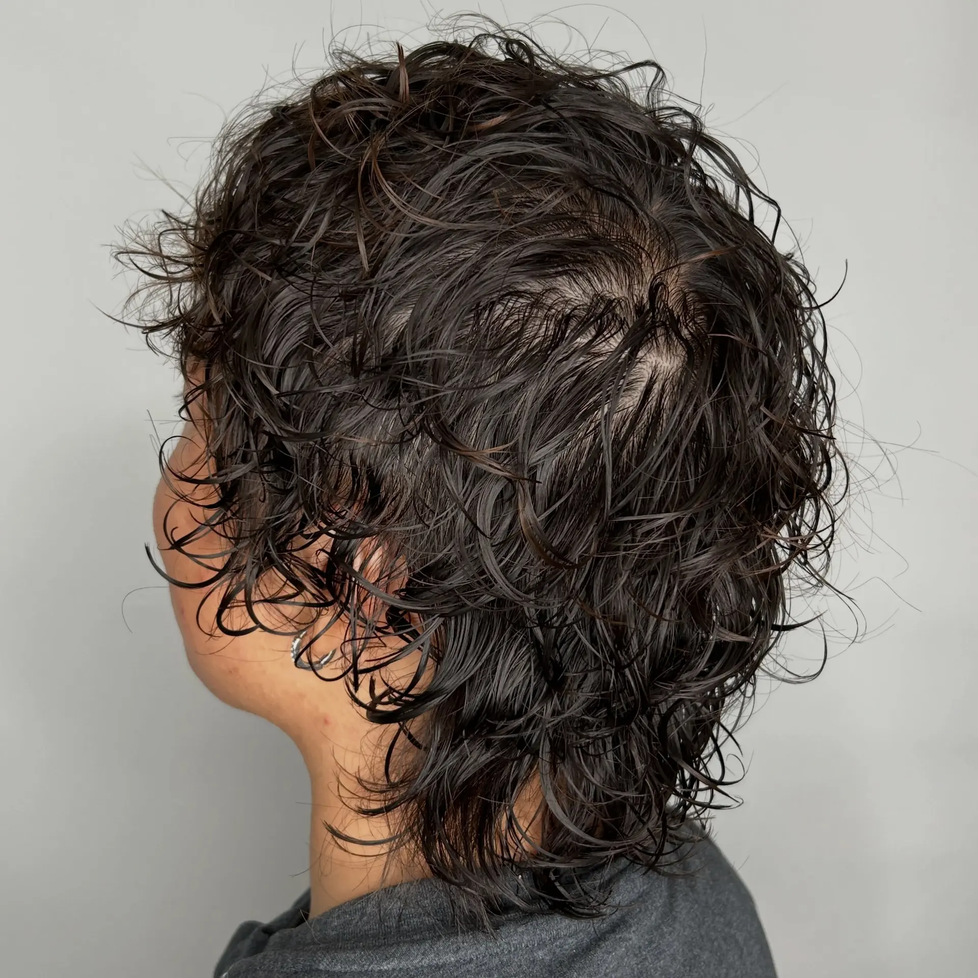 A short, layered cut styled with wet-look permed curls and natural texture around the ears and nape. 1
