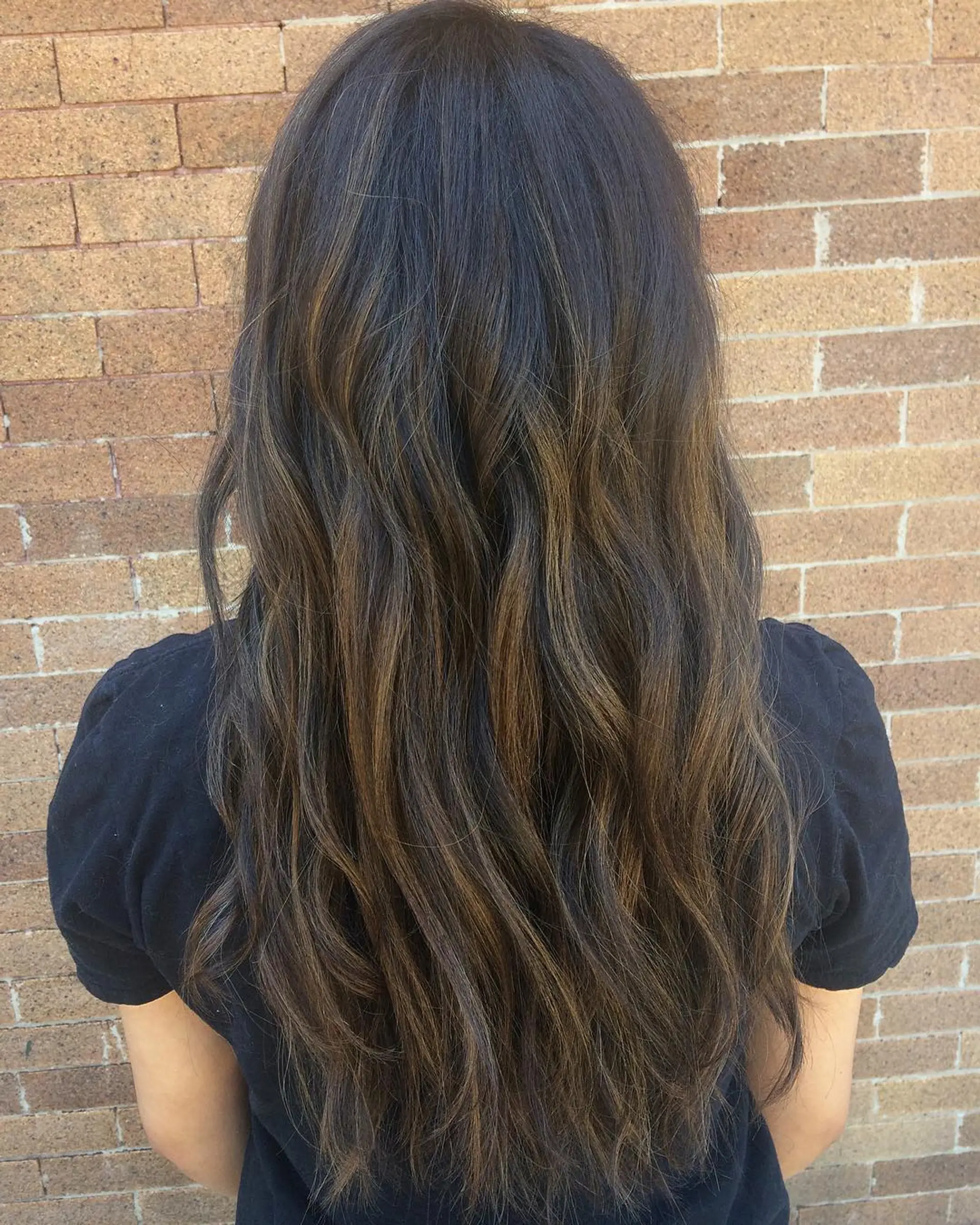 A long wavy brunette hairstyle with subtle caramel balayage highlights for added dimension. 1