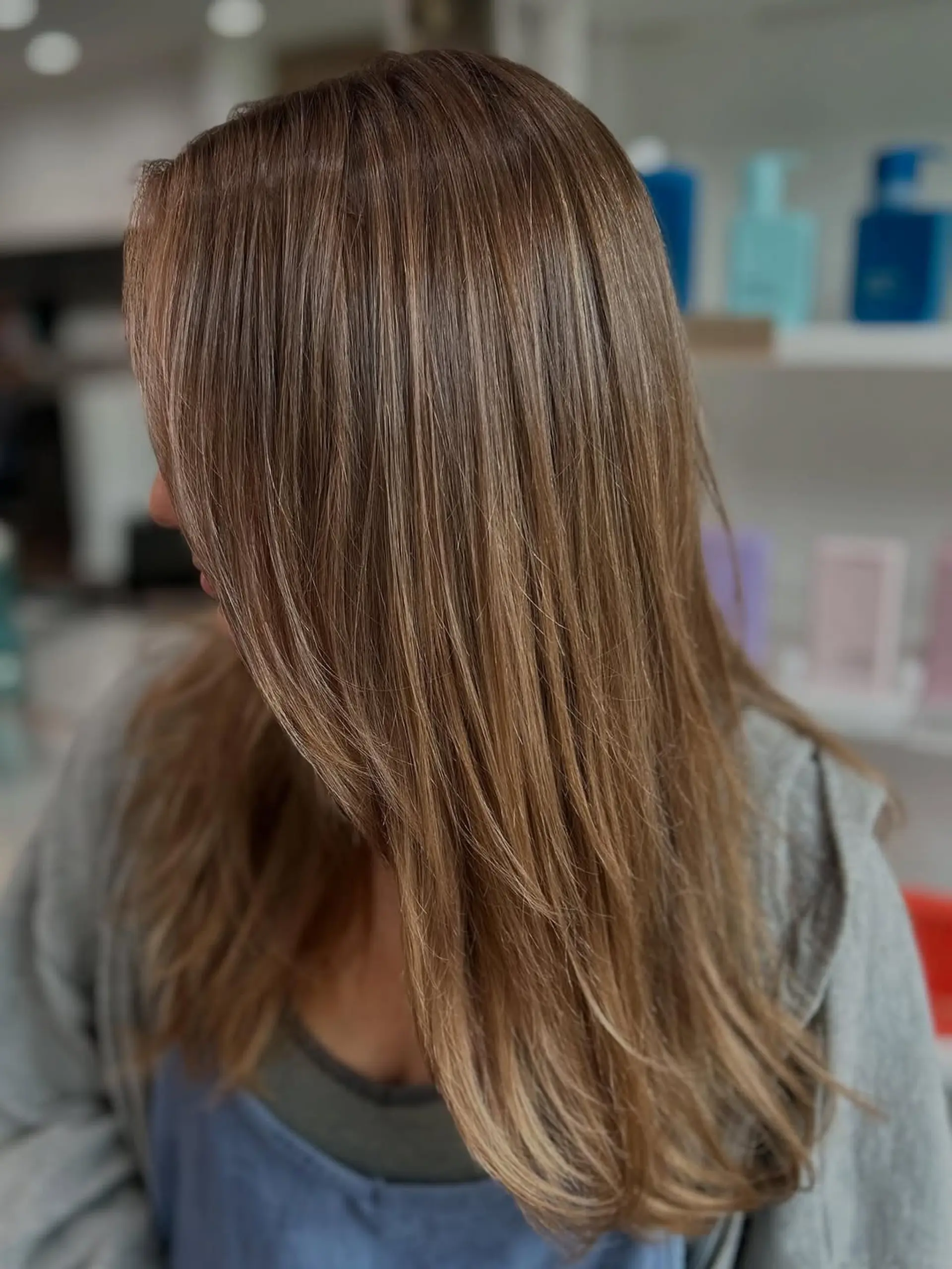 A long, straight hairstyle with seamless layers that create movement and dimension. The style features a mix of light brown base with subtle caramel and bronde highlights. 1