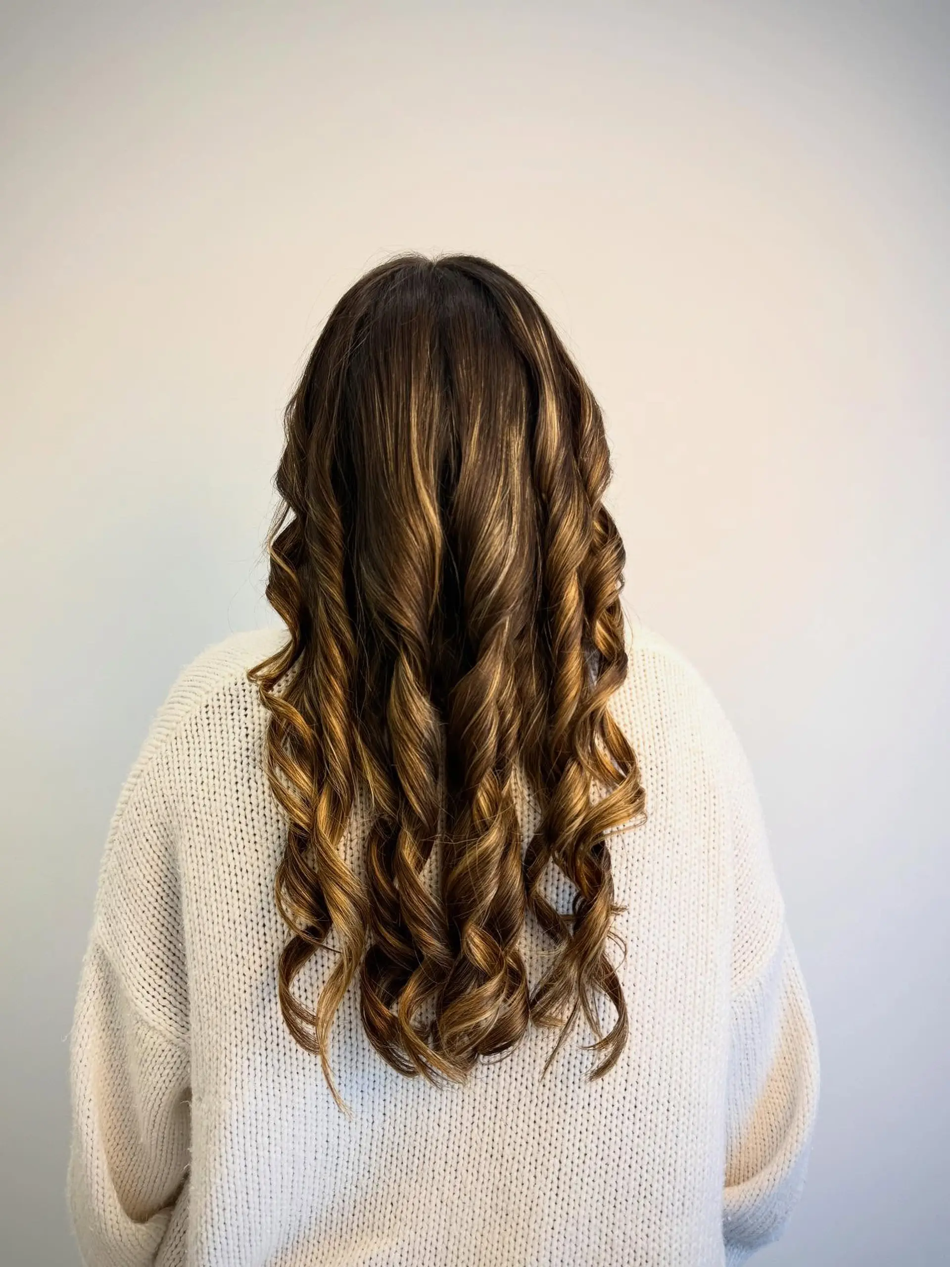 Long brunette hair styled into defined, polished spiral curls with dimensional caramel highlights. 1