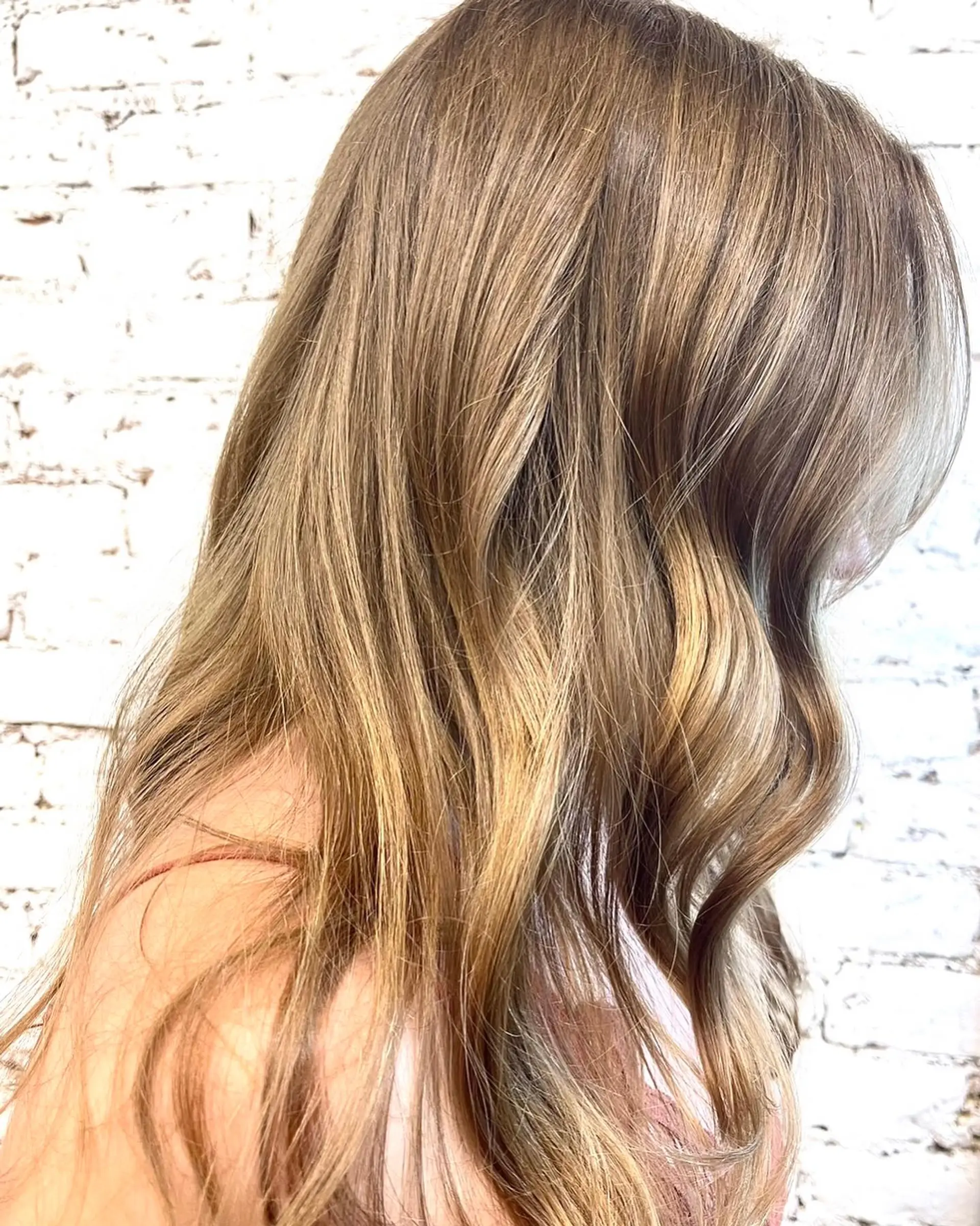 Long warm brown hair enhanced with blended caramel and honey blonde highlights styled in soft, loose waves. 1