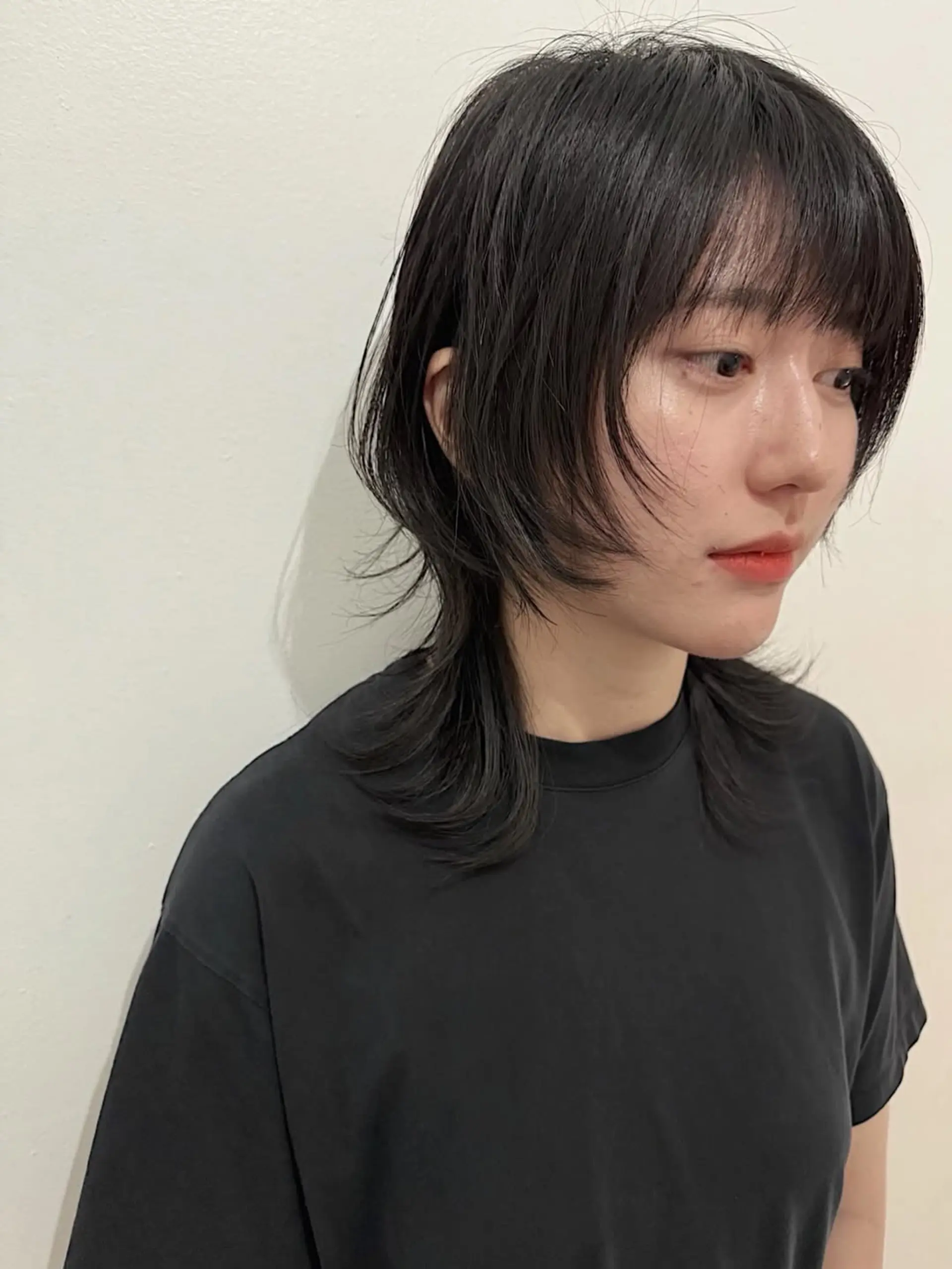 A modern Soft Shullet haircut characterized by choppy, face-framing layers, shorter sides, and a subtly longer back, complemented by delicate wispy bangs. 1