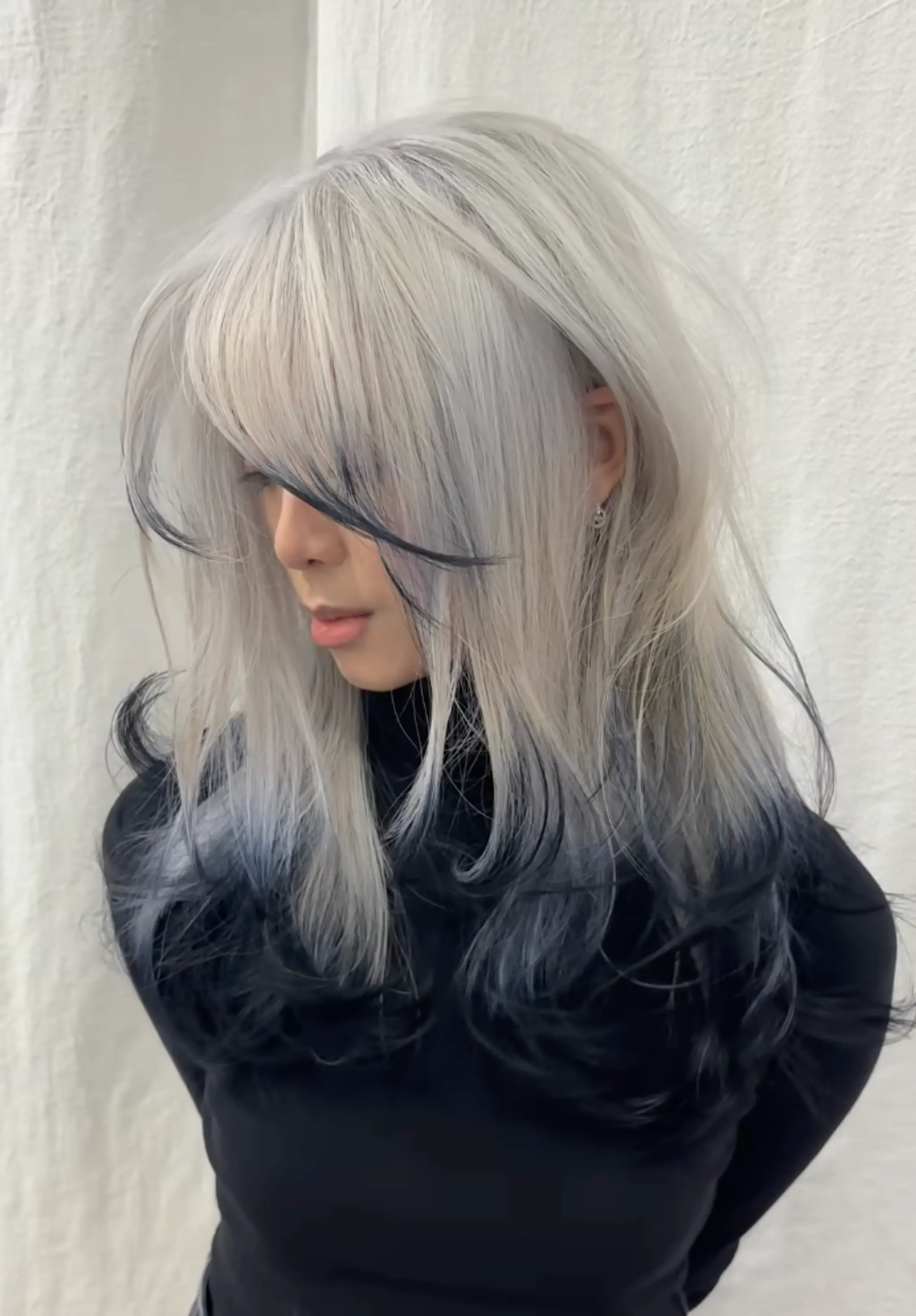 Long, wavy ombre hairstyle with silver transitioning to black, layered with face-framing bangs and textured ends.