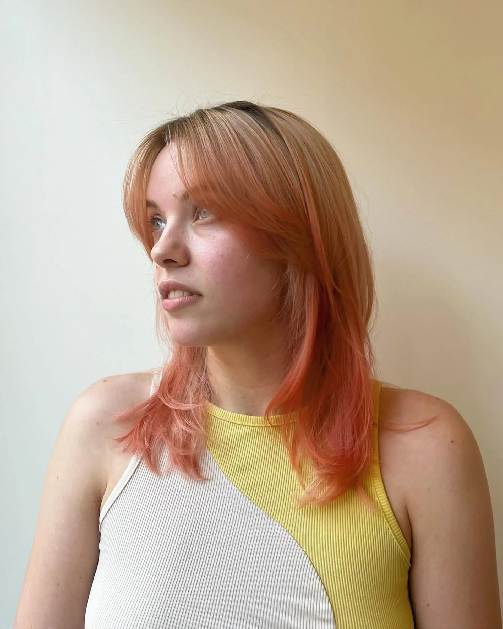 A medium-length wavy hairstyle with layered cuts and face-framing bangs, featuring strawberry blonde and peach colors. 2