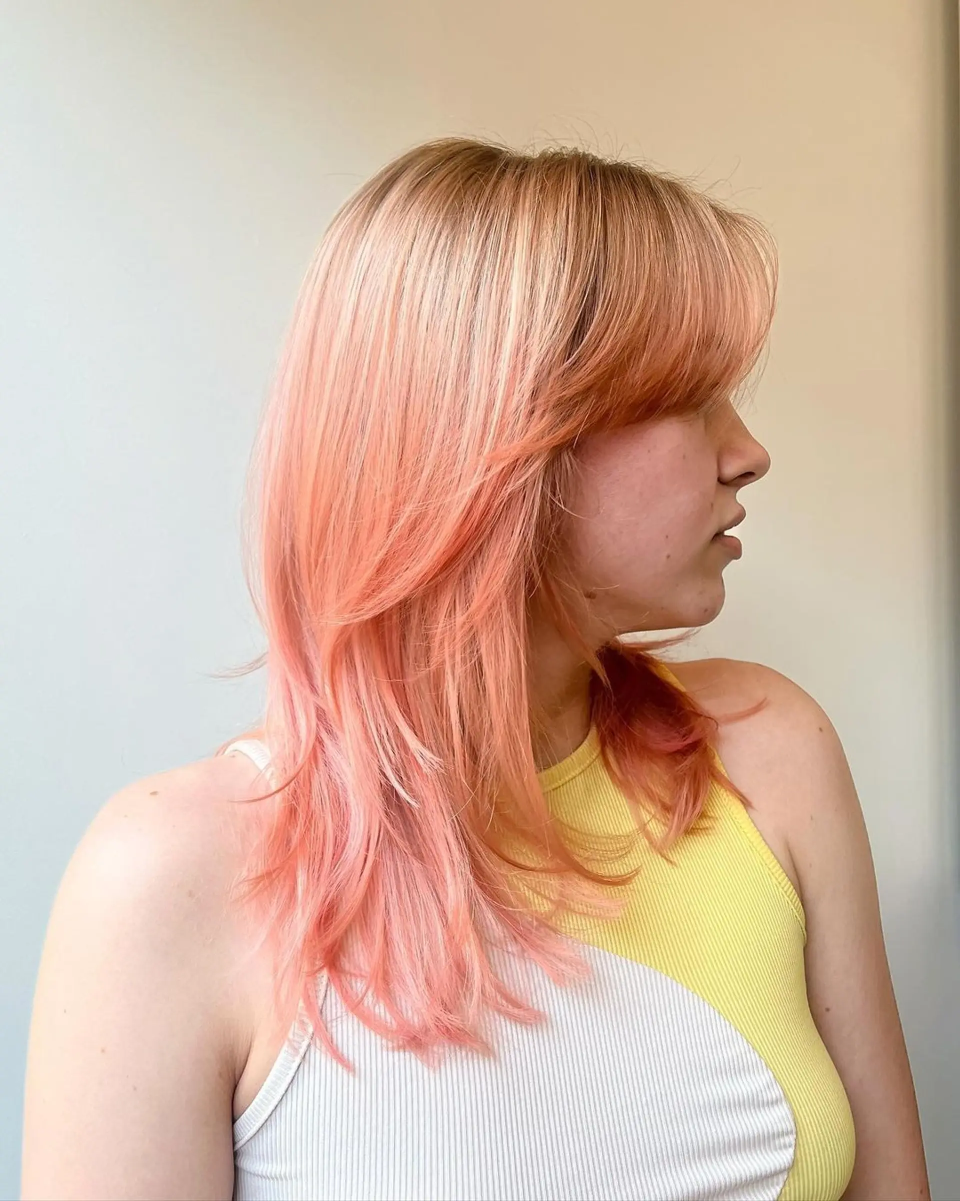 A medium-length wavy hairstyle with layered cuts and face-framing bangs, featuring strawberry blonde and peach colors. 1