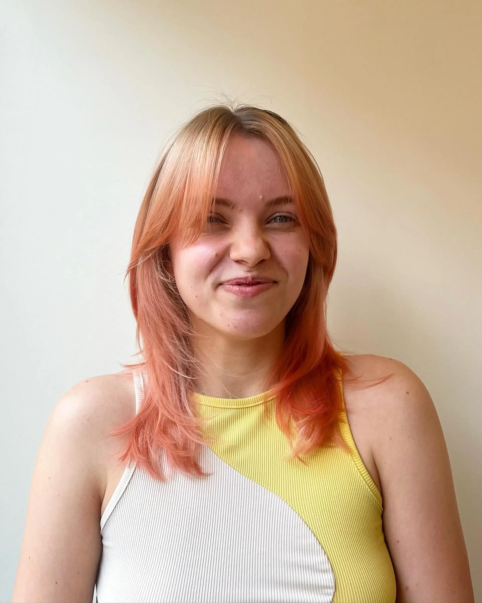 A medium-length wavy hairstyle with layered cuts and face-framing bangs, featuring strawberry blonde and peach colors. 3