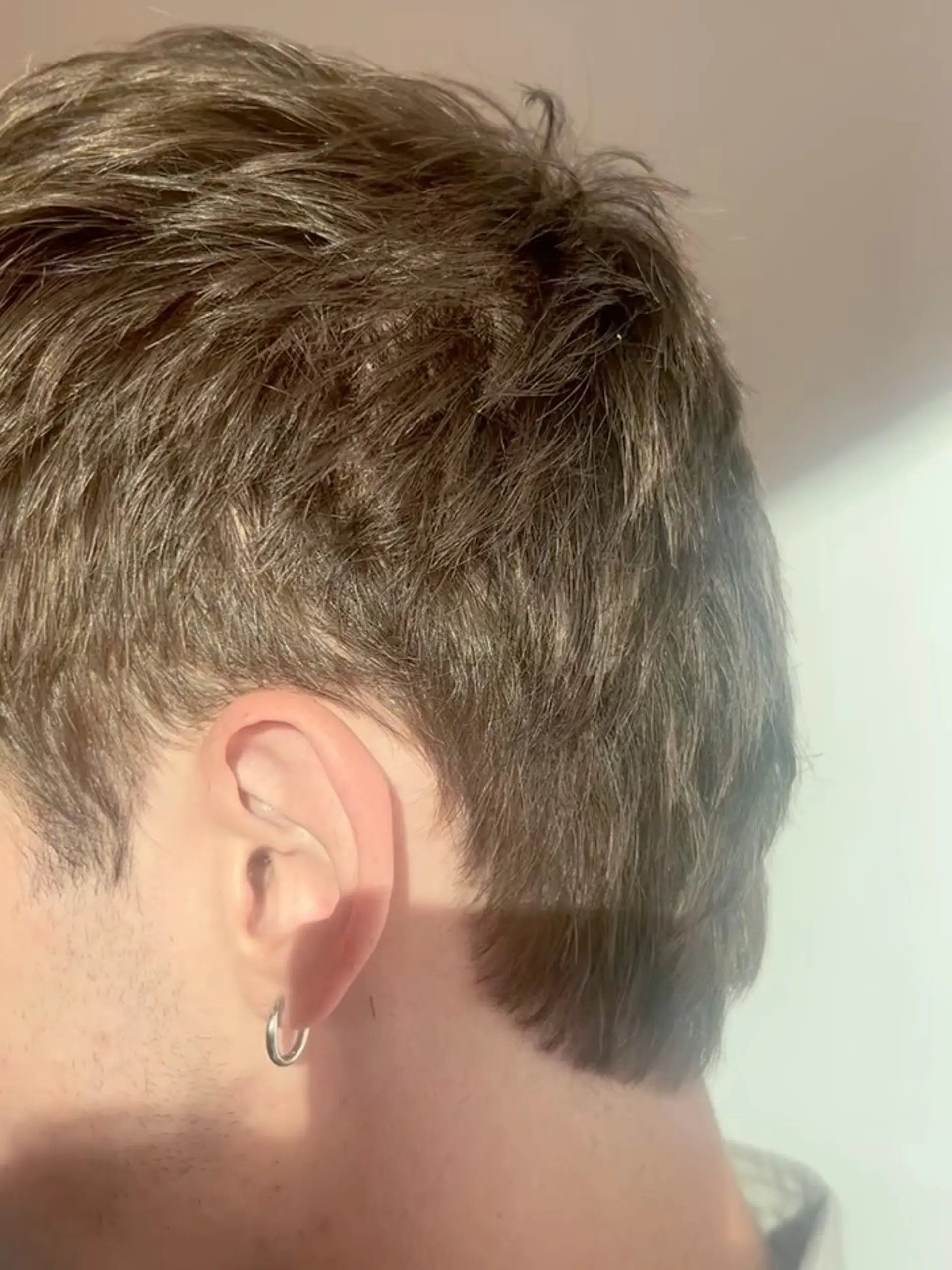 A modern short haircut featuring heavy texture on top with soft taper detailing around the ear. 1