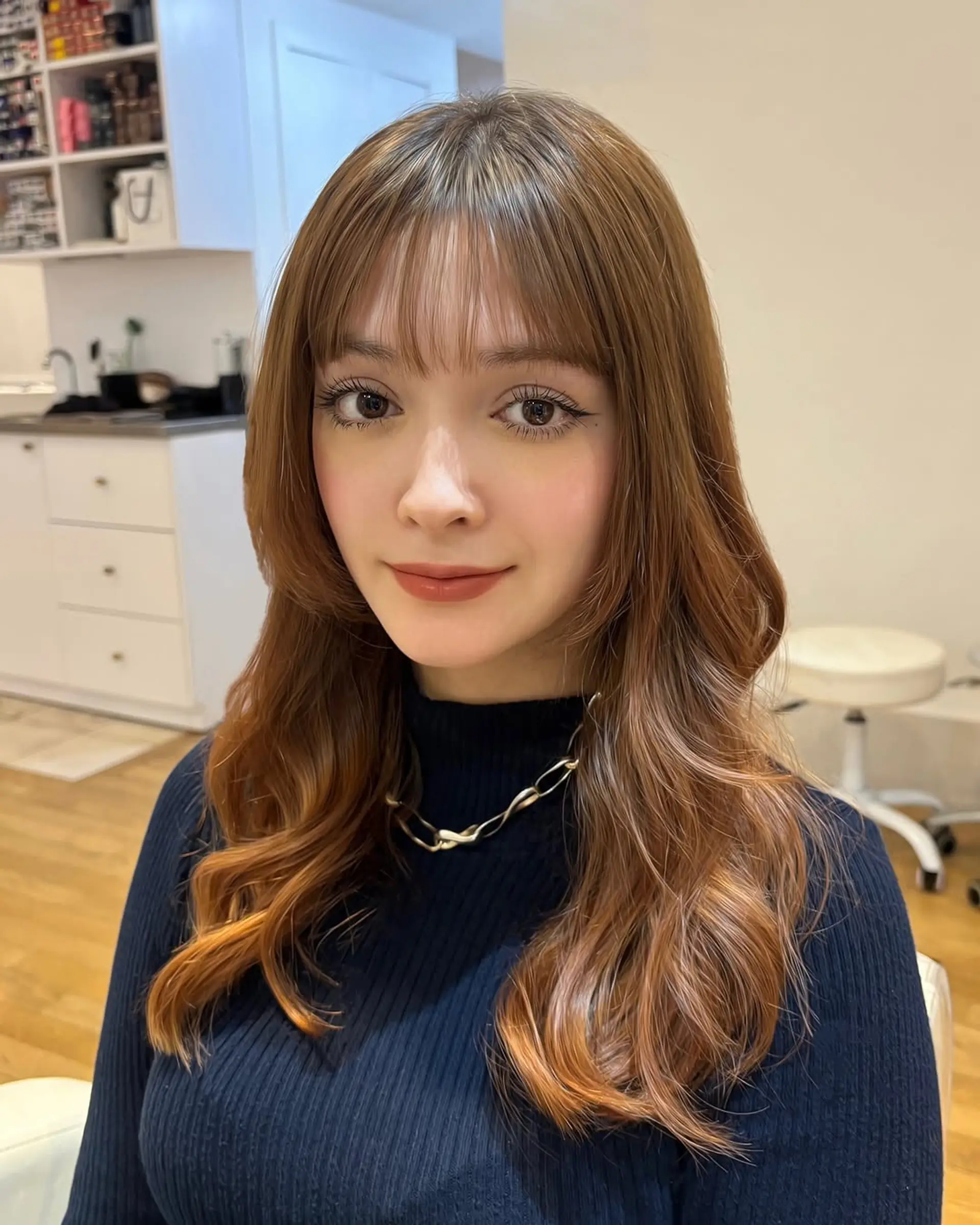 Long, layered hair with face-framing layers and soft waves, complemented by stylish Bardot bangs. 1