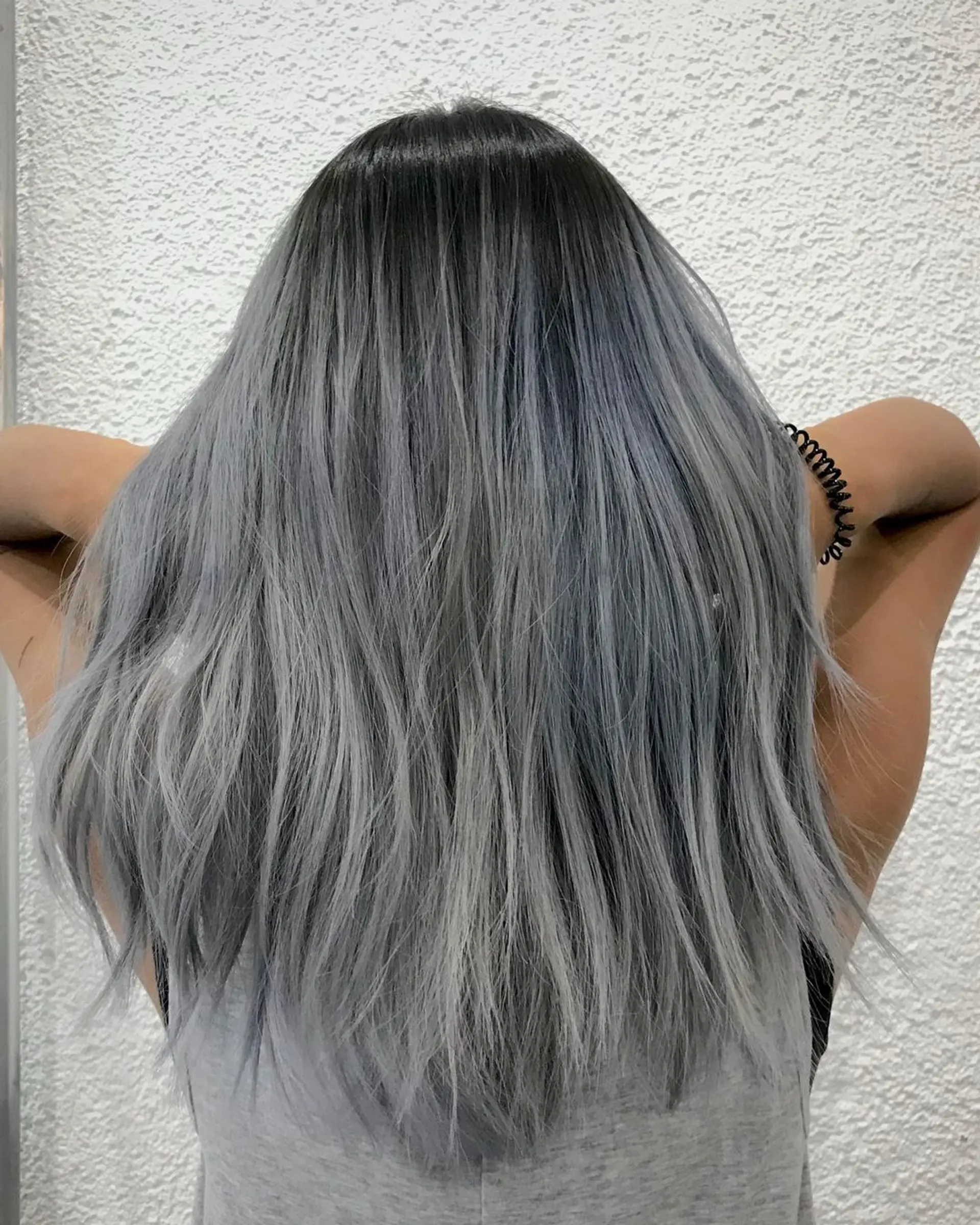 The hairstyle is a long, straight ombre with dark roots transitioning to a silvery-gray hue. It features layers for added volume and dimension, exuding a cool, frosted appearance. 1