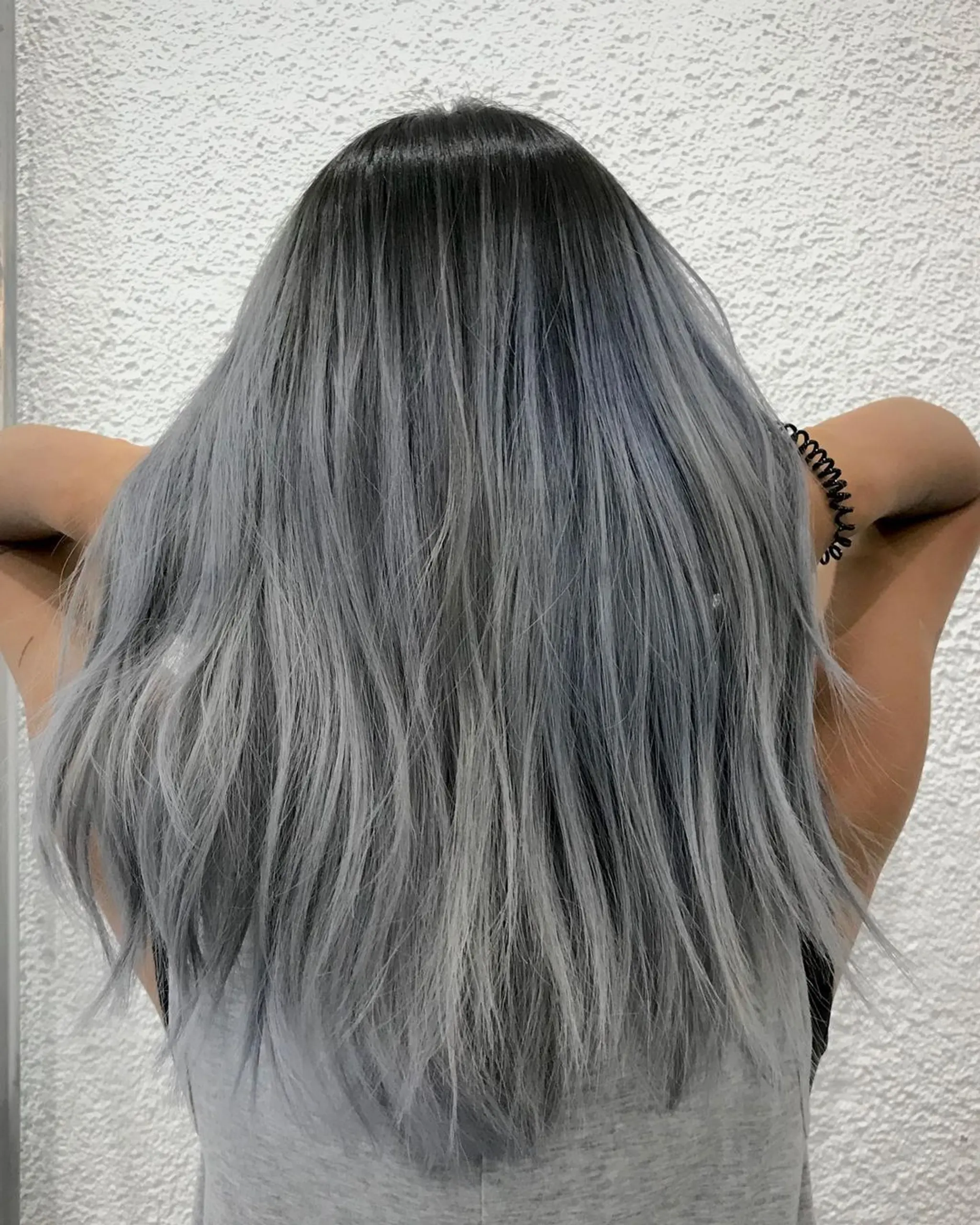 The hairstyle is a long, straight ombre with dark roots transitioning to a silvery-gray hue. It features layers for added volume and dimension, exuding a cool, frosted appearance.