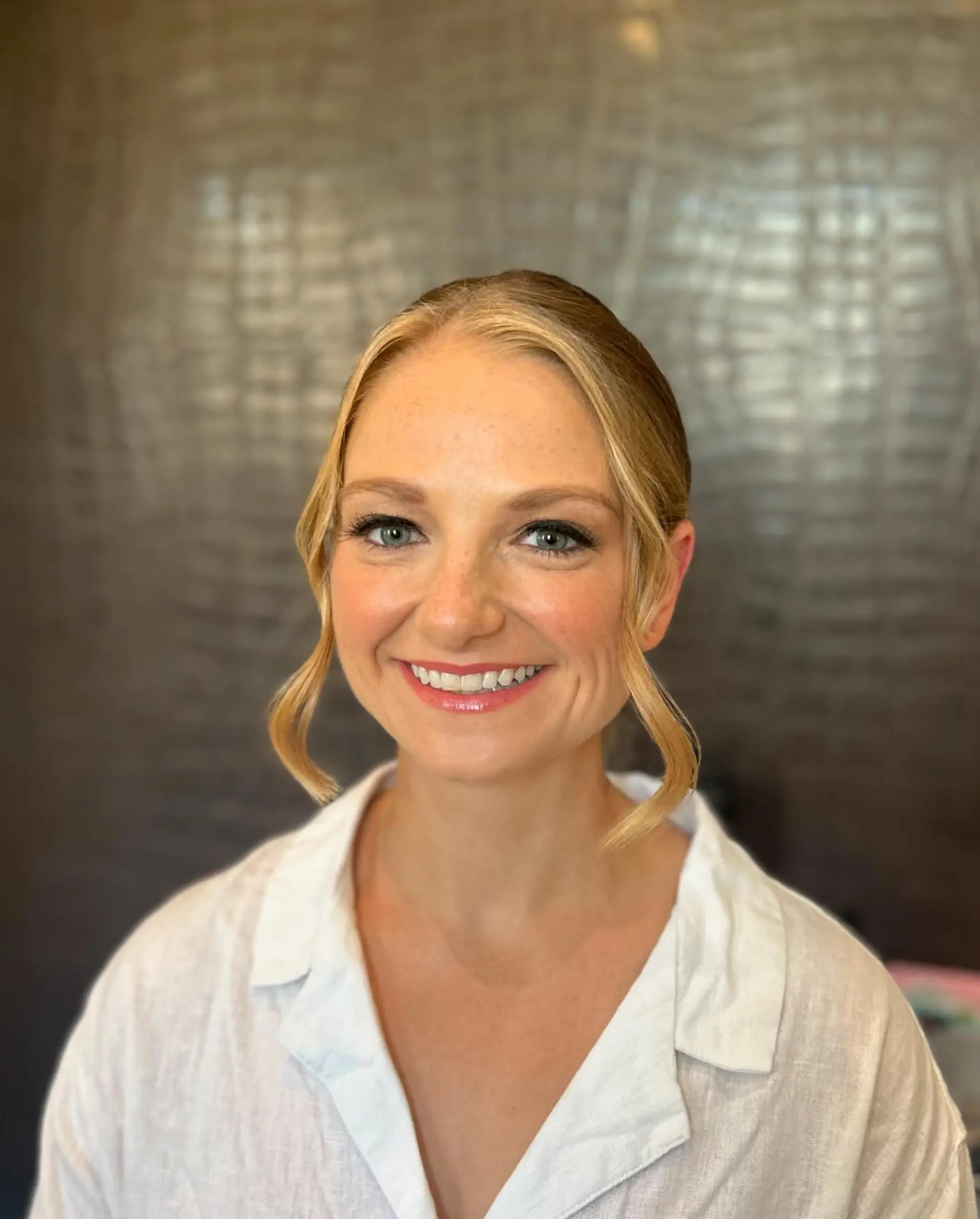 An elegant bridal updo with a clean center part and soft, waved face-framing pieces. 1